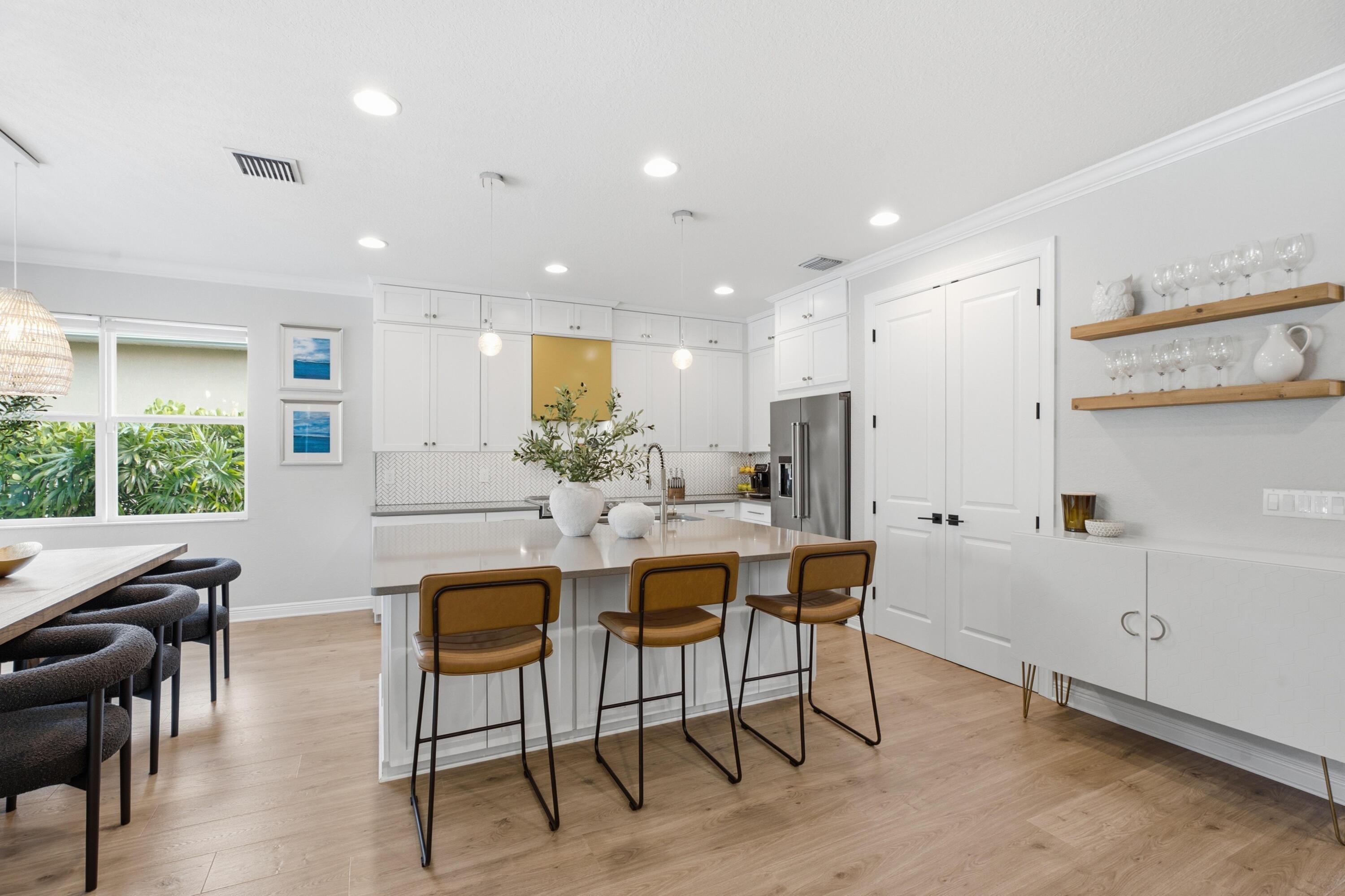 Bright white kitchen with a large island, three brown bar stools, and stainless steel appliances.