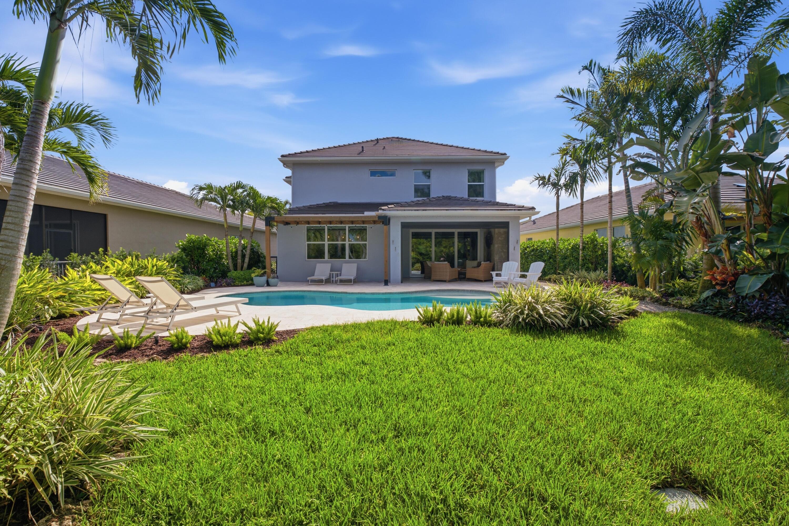 Two-story home behind a backyard pool, with patio seating, palms, and a wide lawn.