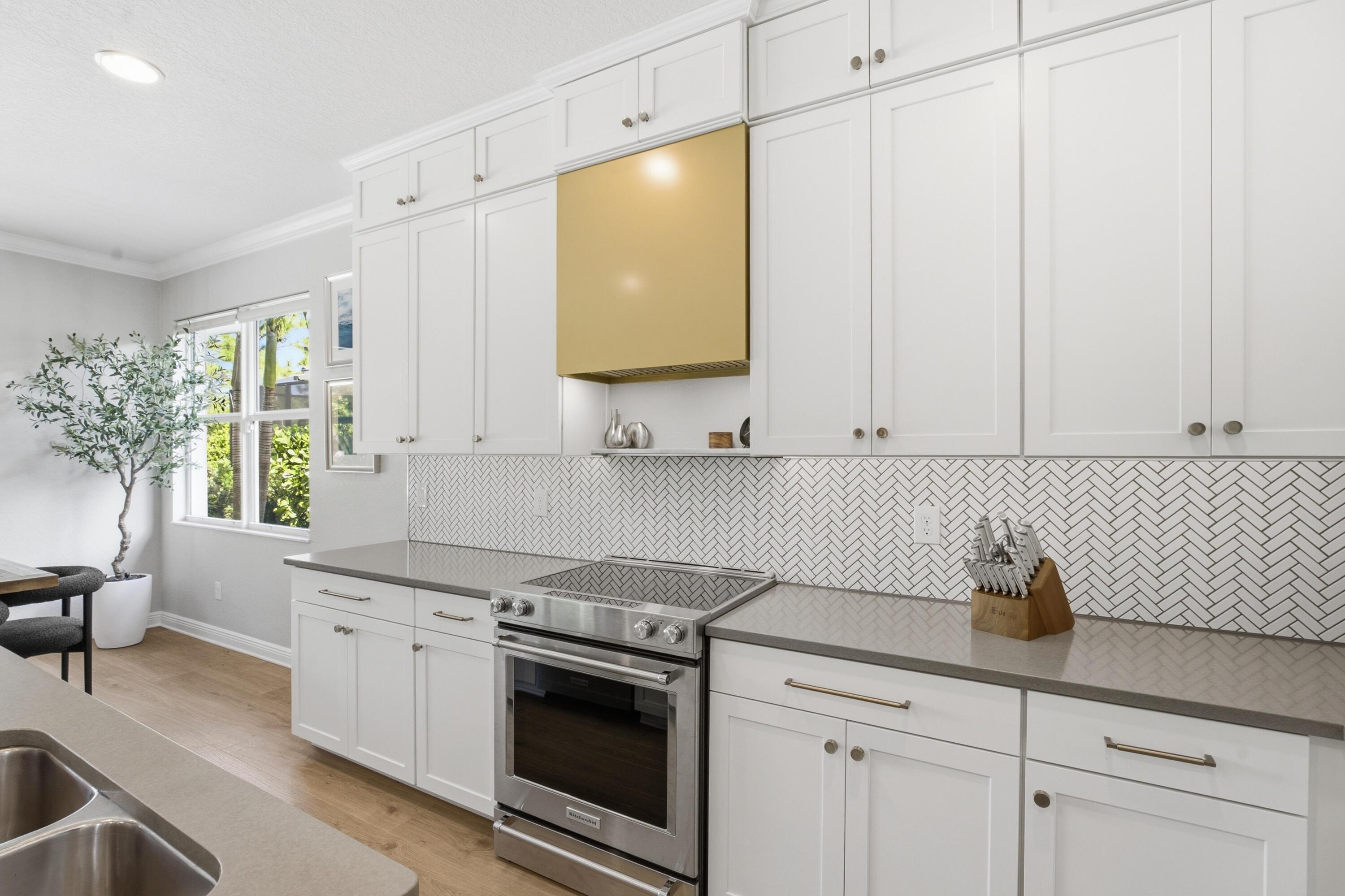 Bright white kitchen with herringbone backsplash, gold range hood, and stainless steel range.
