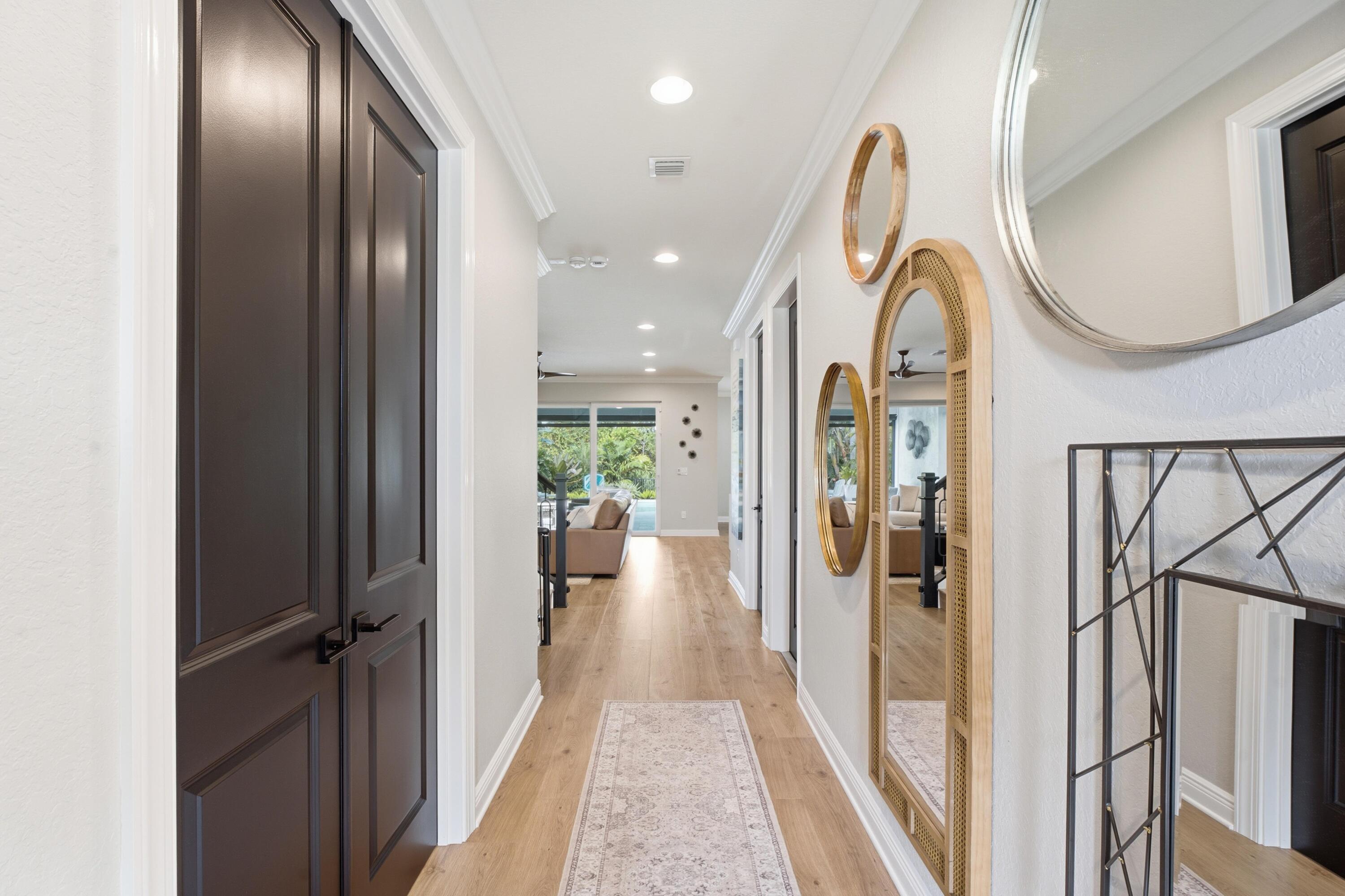 Furnished hallway with light wood floors, a pale runner, decorative mirrors, and a view into the living room.
