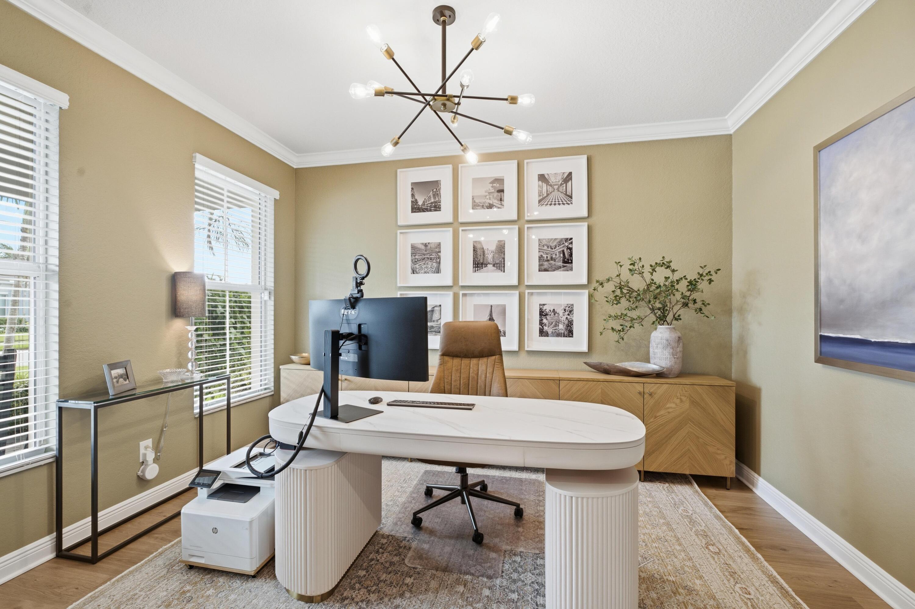 Furnished home office with a white oval desk, computer, tan chair, and framed prints.