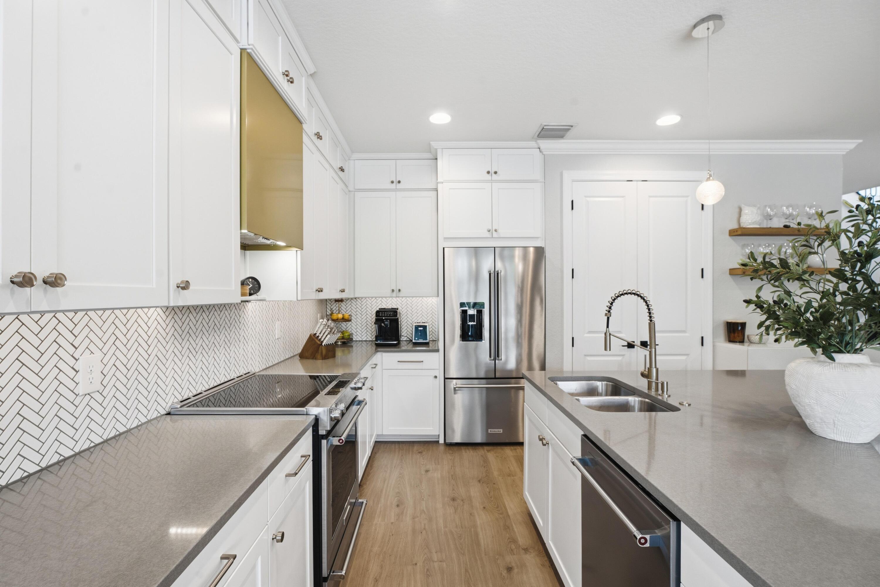Kitchen with white cabinets, herringbone backsplash, stainless appliances, and a large island sink.
