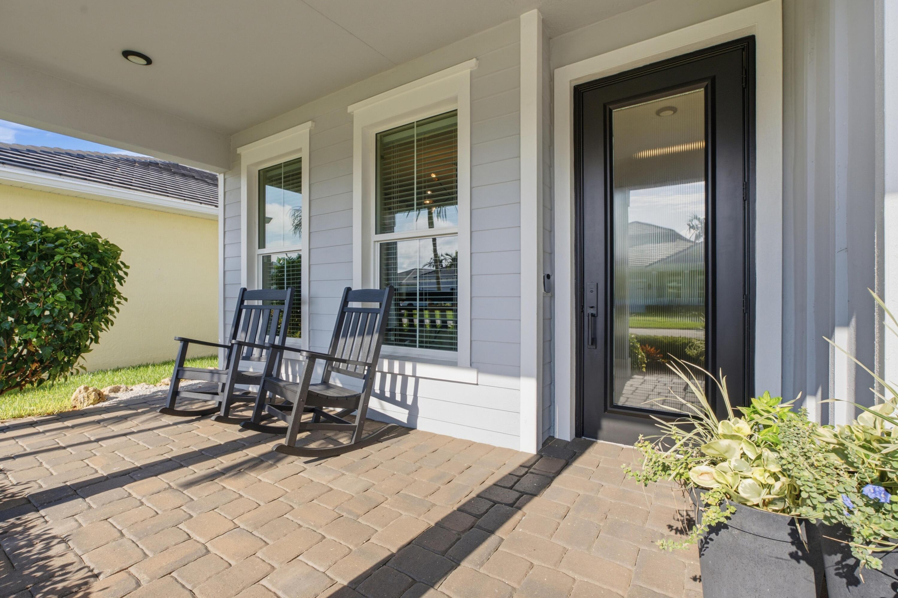 Front porch with a black glass-paneled door, two rocking chairs, and a paved patio.