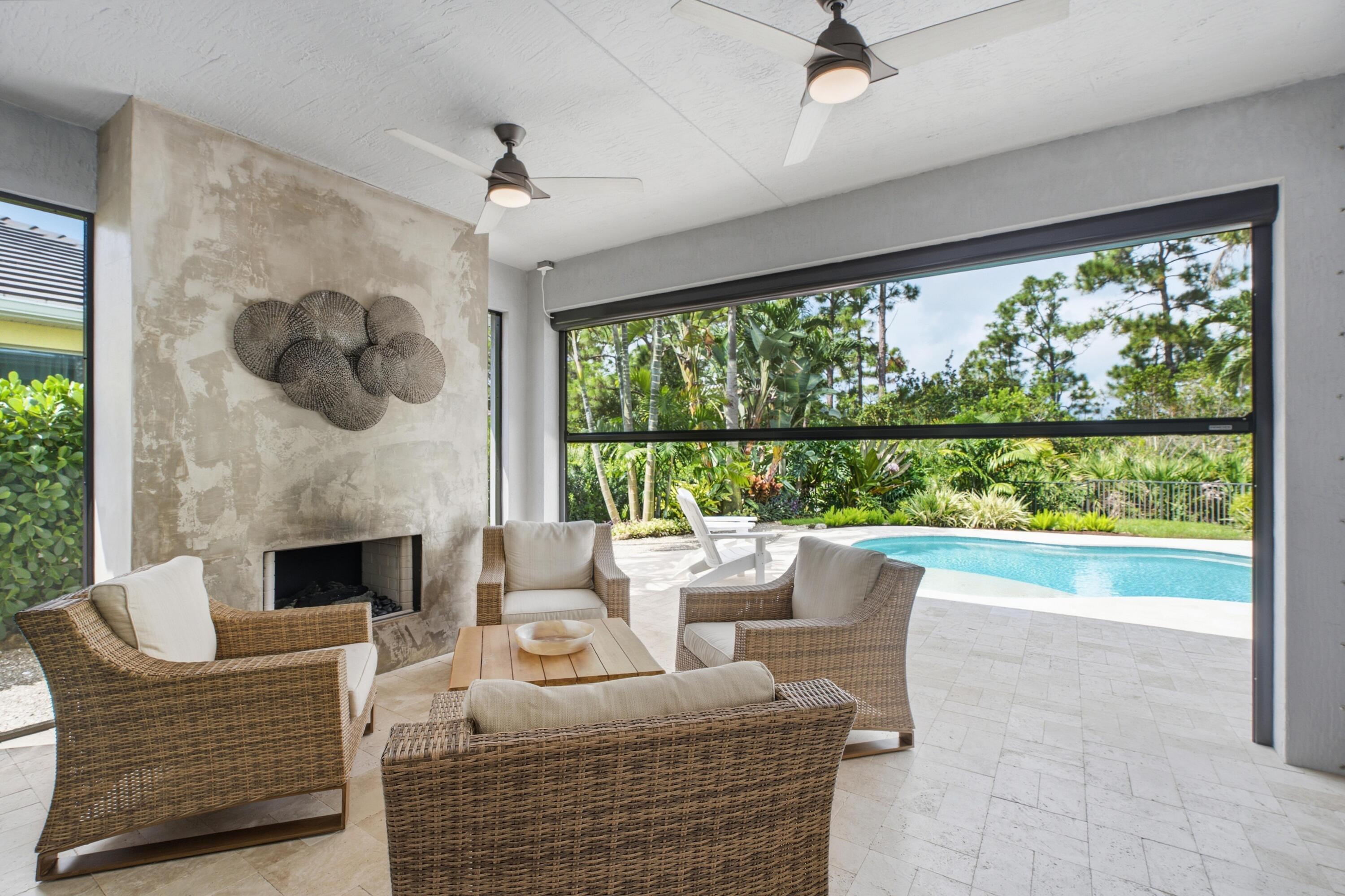 Covered patio with wicker seating and fireplace opening onto a pool and tropical garden.