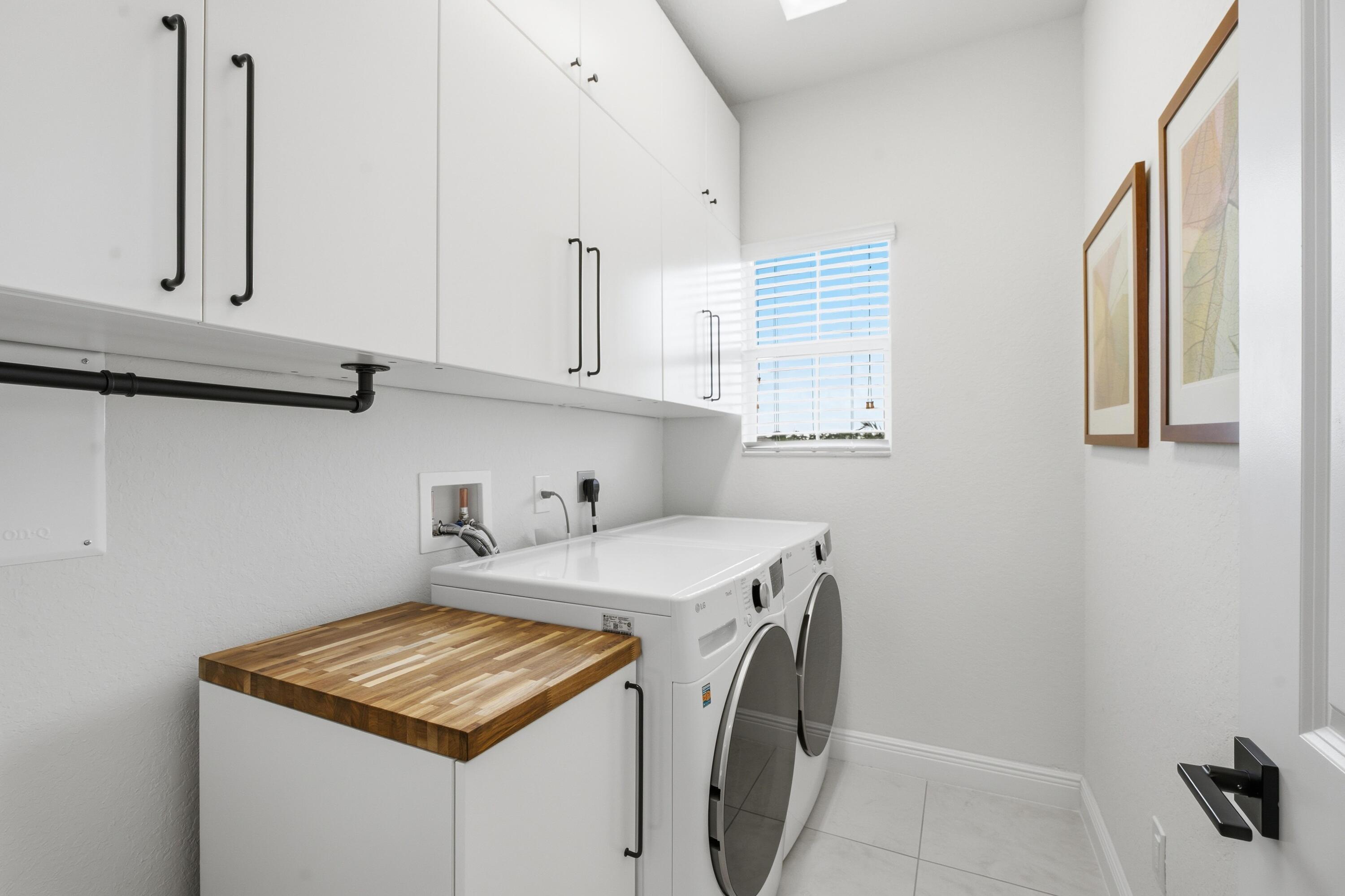 Laundry room with white cabinets, front-loading washer and dryer, and a butcher-block counter.