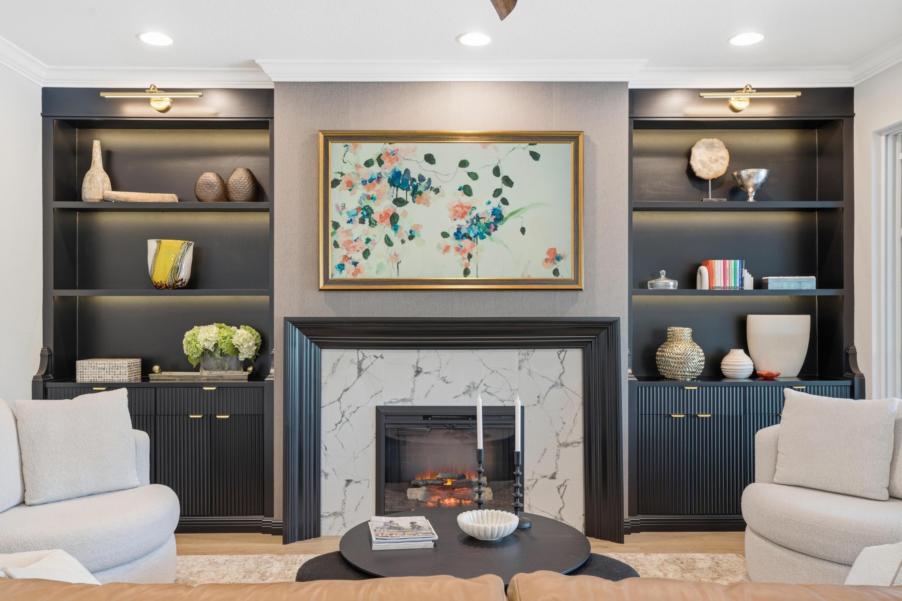 Living room with a marble fireplace, dark built-in shelves, and light upholstered chairs.