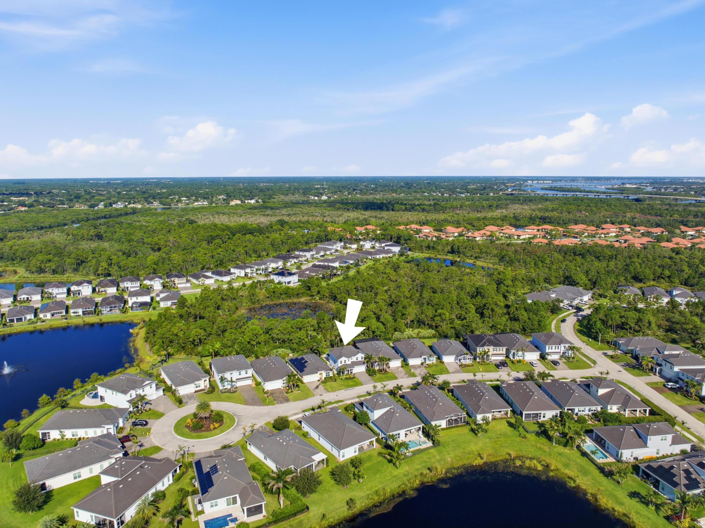Aerial neighborhood view with an arrow marking a home beside ponds and a wooded preserve.