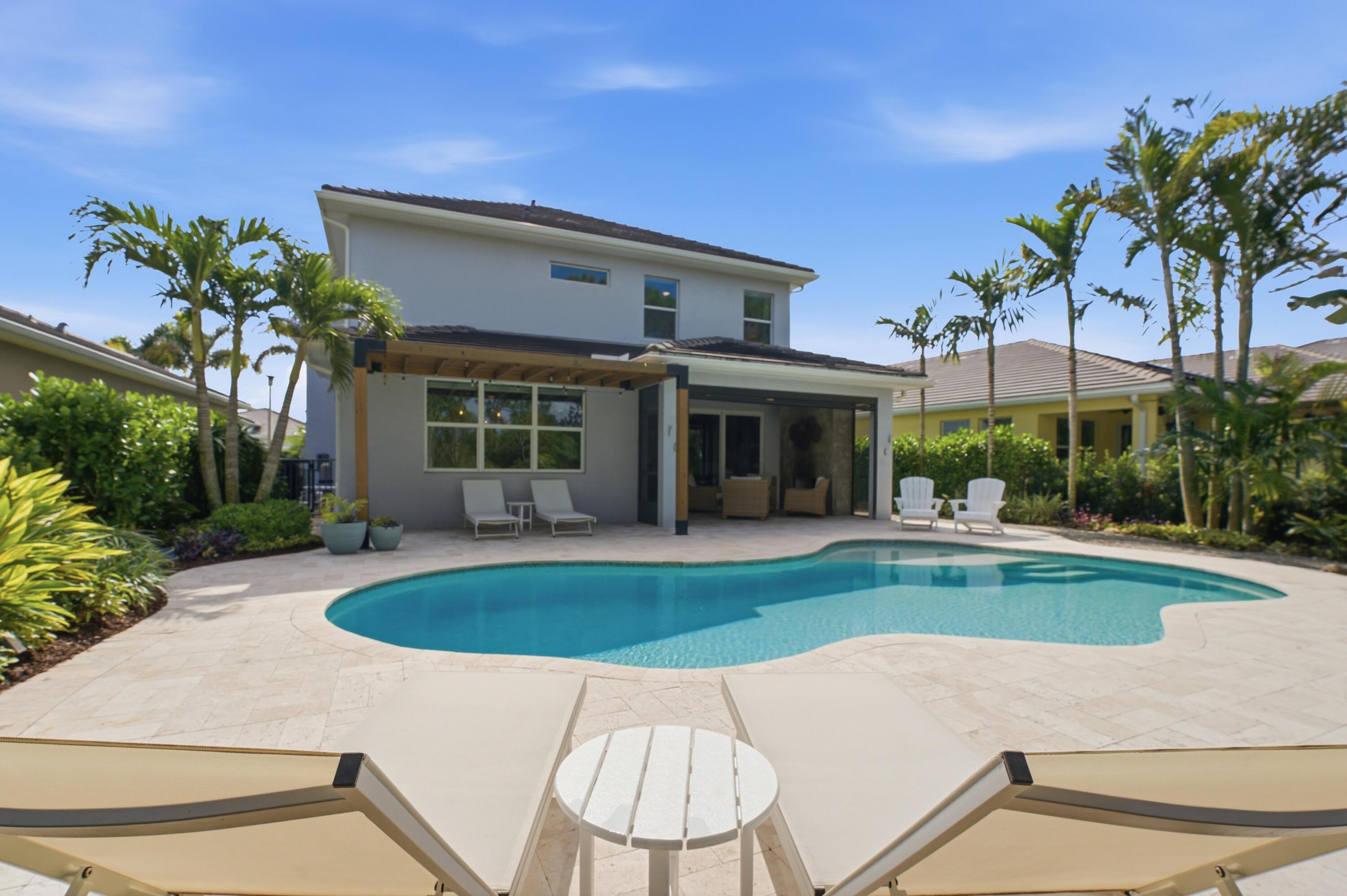Two-story home behind a freeform pool, with a covered patio and tropical landscaping.