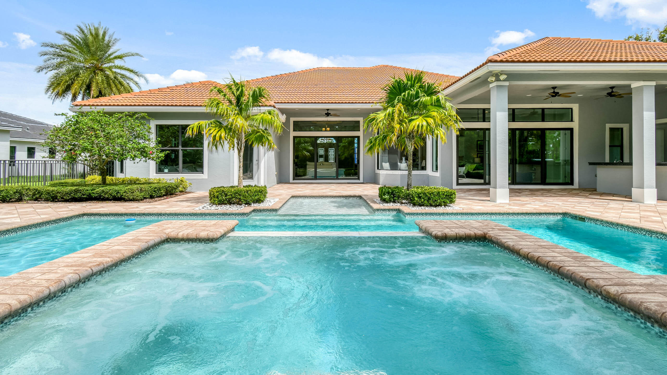 Backyard pool and raised spa in front of a single-story home with a covered patio and palm trees.