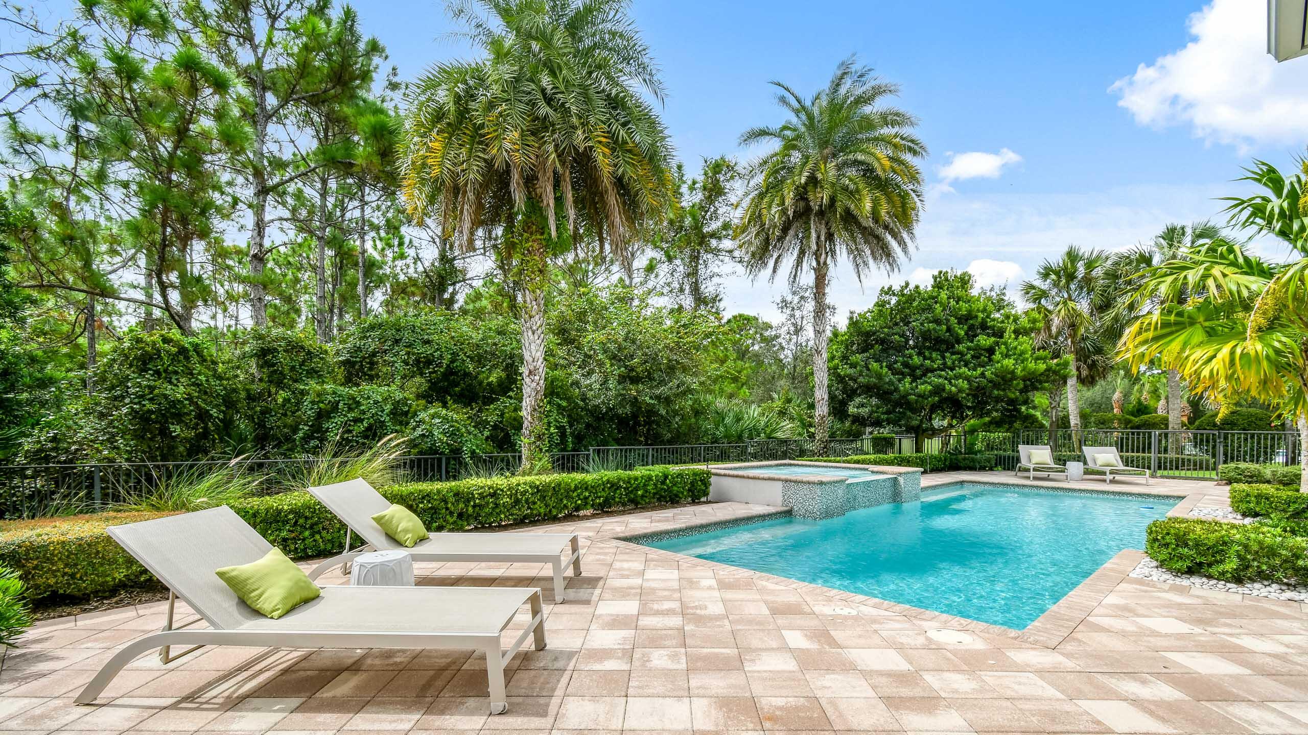 Backyard pool and raised spa surrounded by palms, tropical landscaping, and patio loungers.