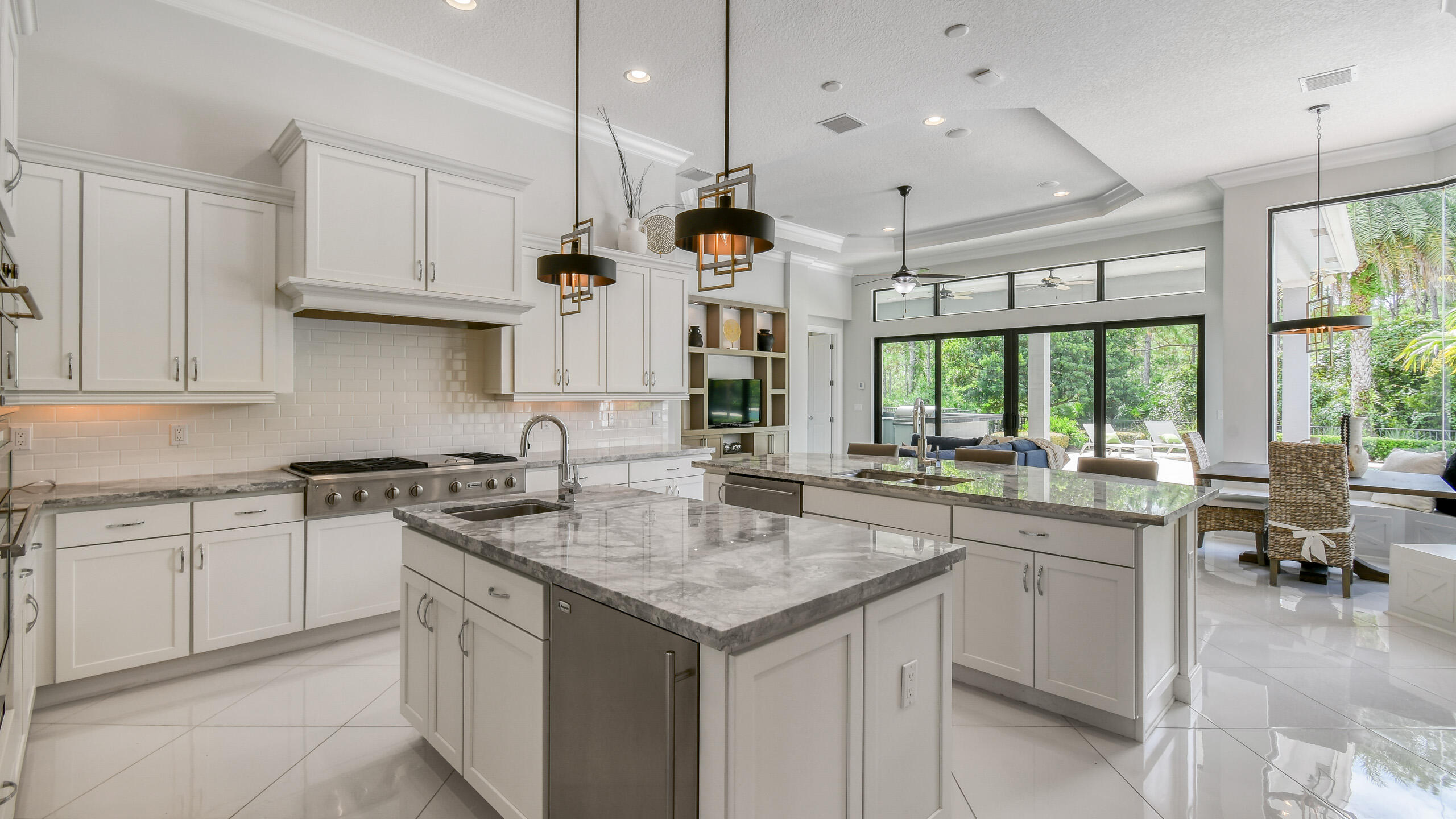 Open-plan kitchen with a large stone island, white cabinetry, and windows overlooking greenery.