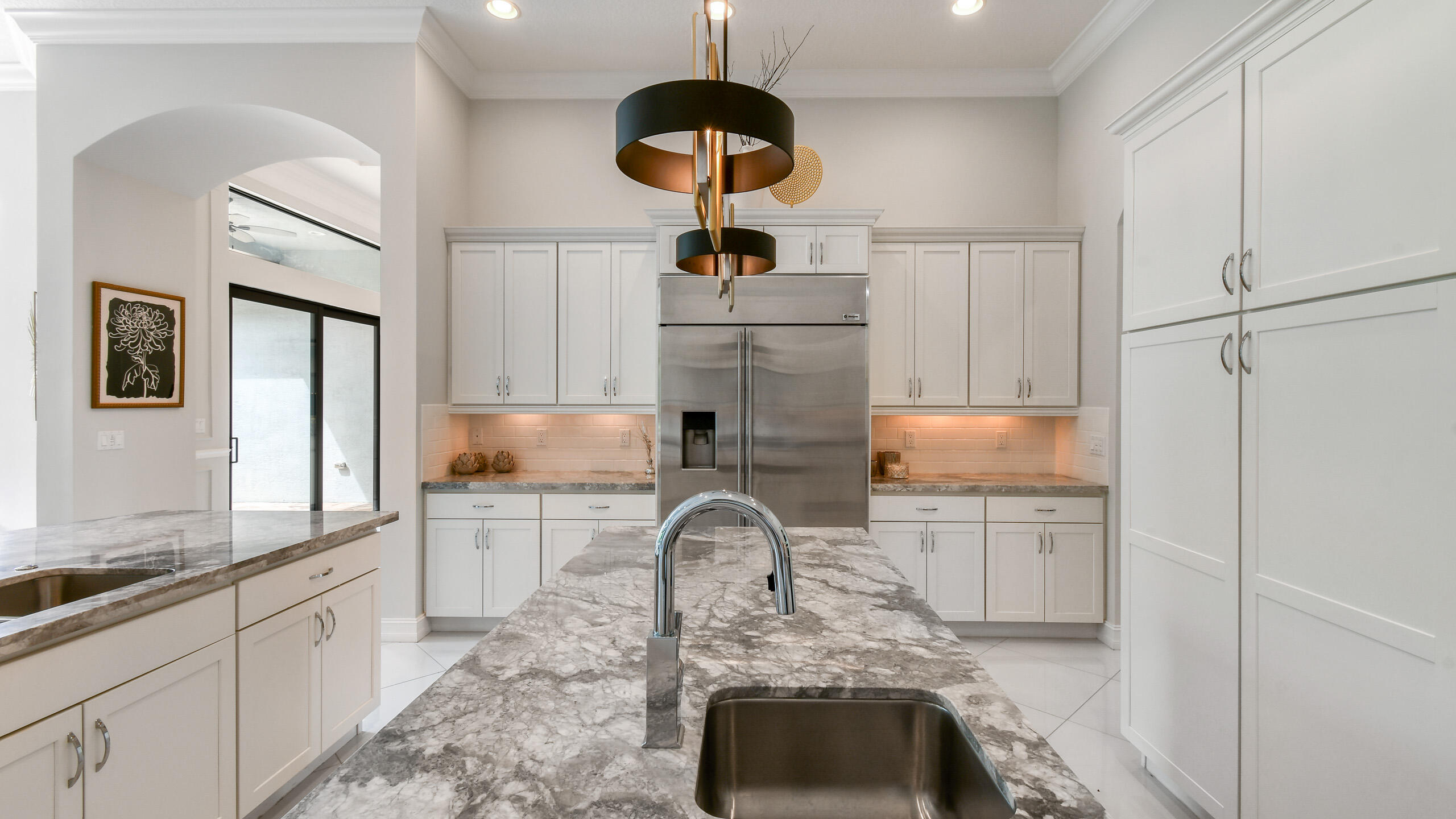 Modern kitchen with white cabinets, stainless refrigerator, and a large stone island with sink.