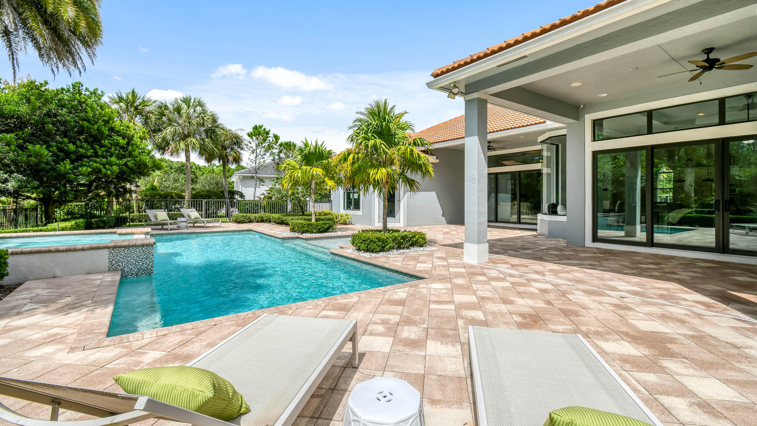 Backyard pool and tiled patio with lounge chairs, palm trees, and a covered terrace.