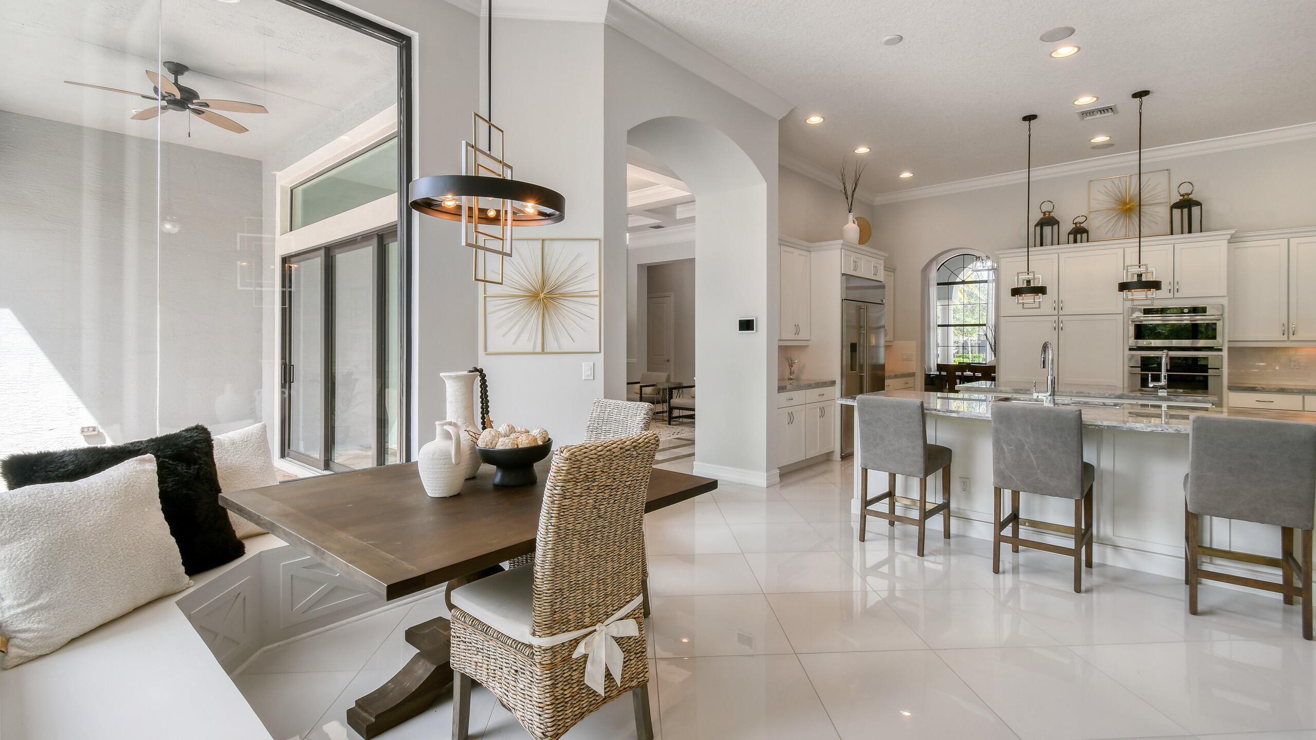 Open-plan kitchen and dining area with white cabinets, marble island, and woven dining chairs.