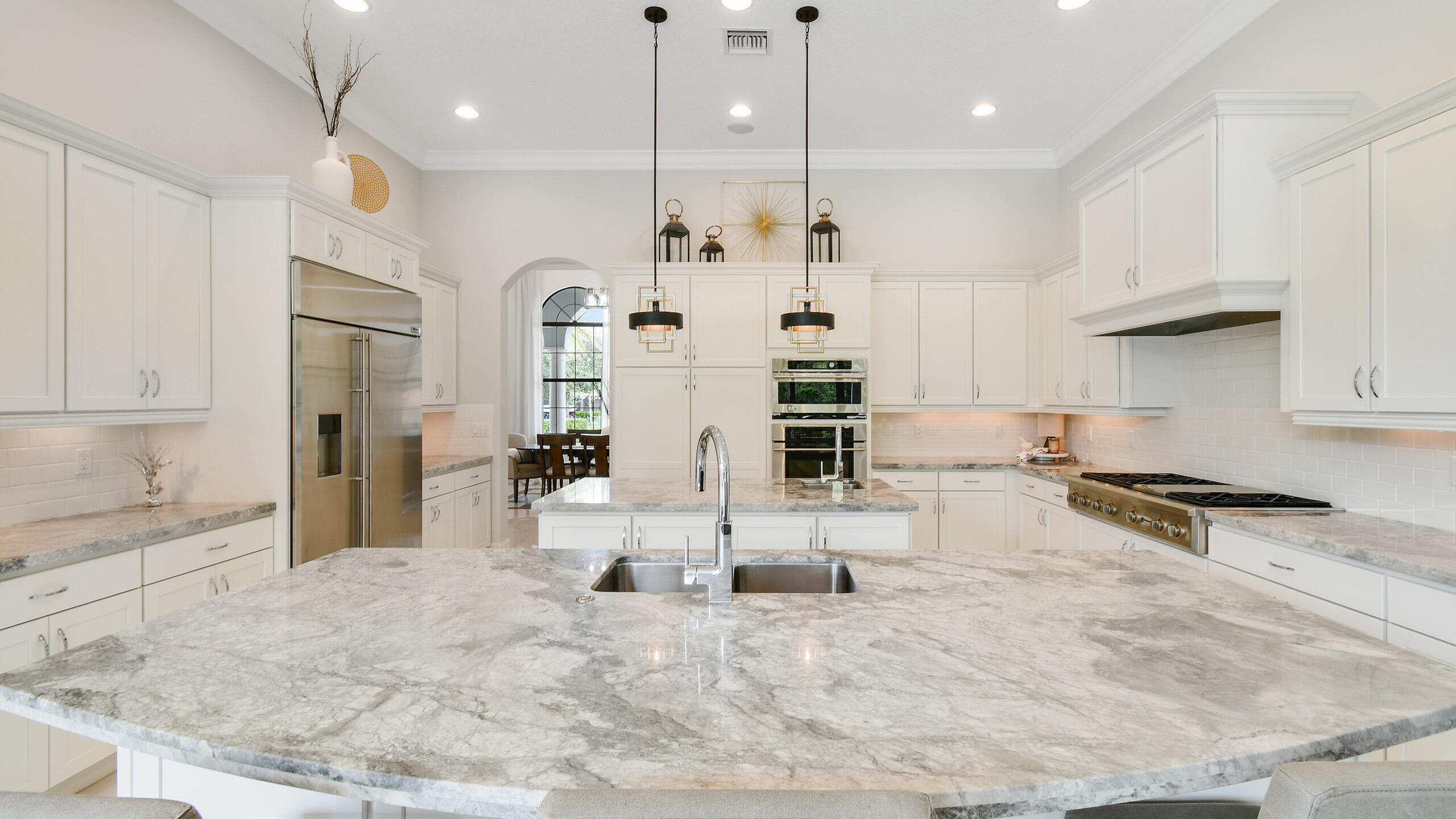 Spacious white kitchen with a large veined stone island, double sink, stainless appliances, and pendant lights.