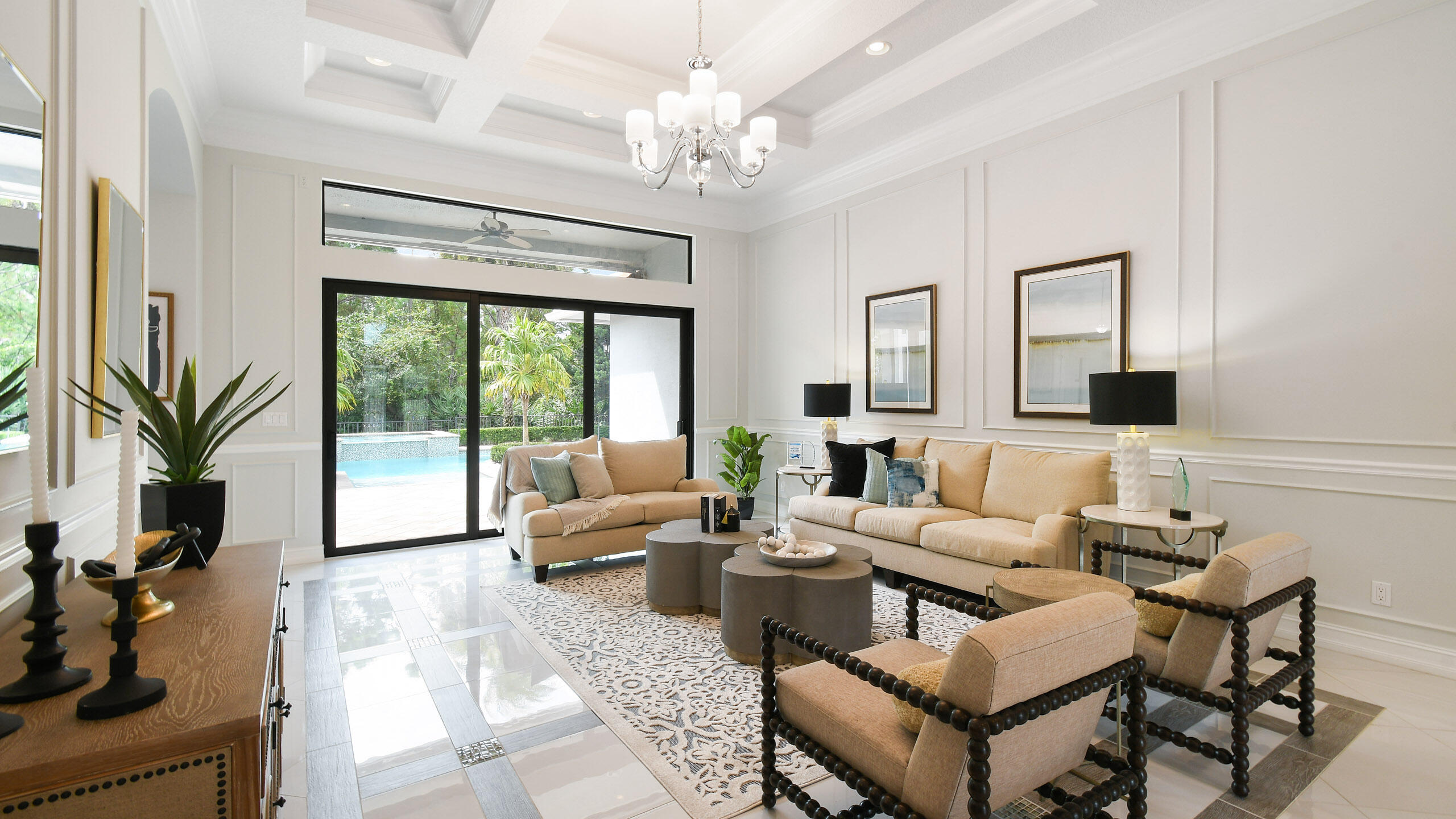 Furnished living room with beige seating, a coffered ceiling, and sliding doors overlooking the pool.