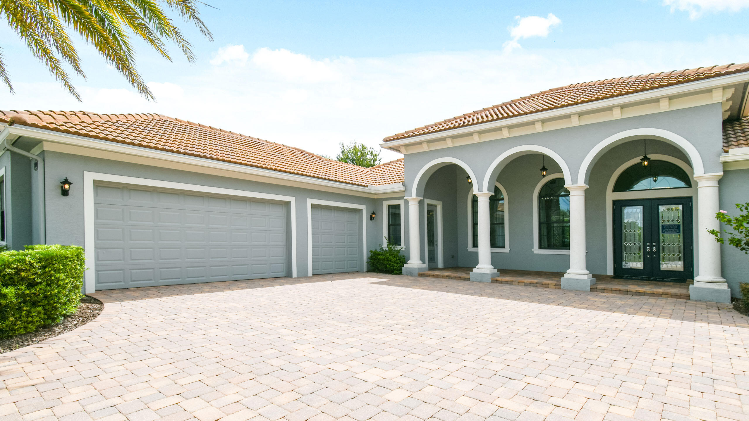 Gray stucco home with a terracotta tile roof, arched entry, and broad paver driveway.
