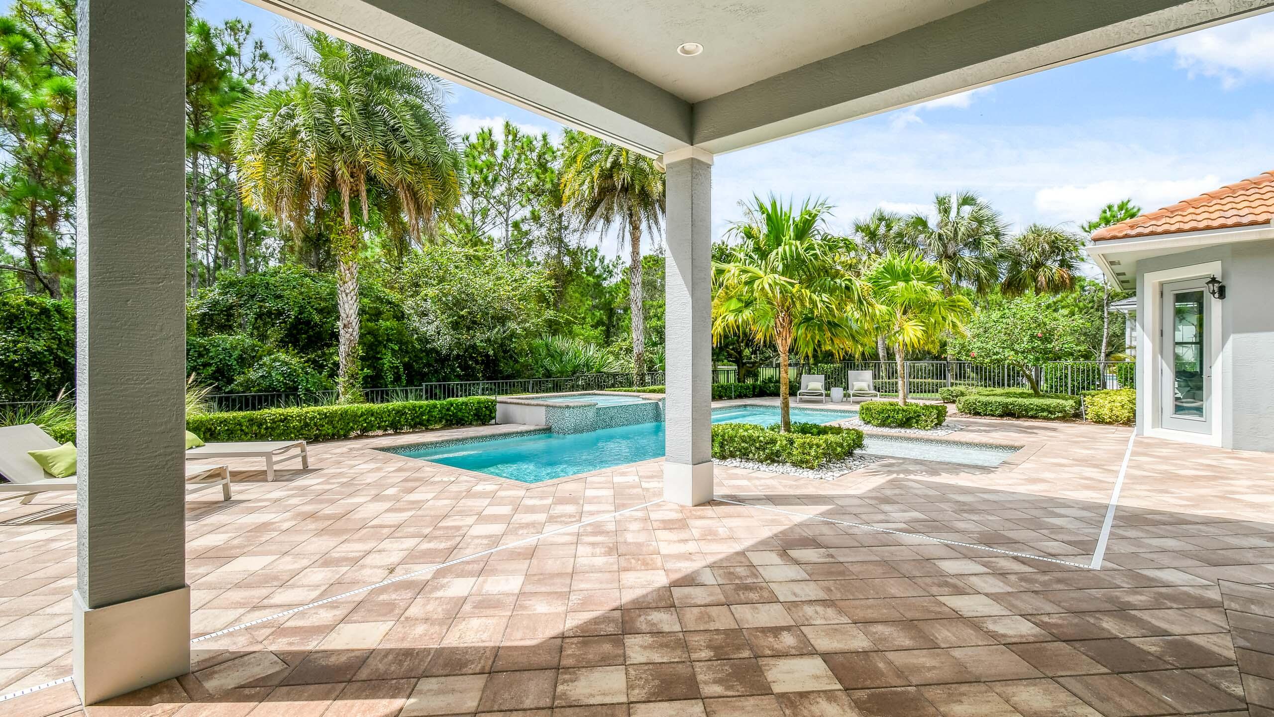 Covered patio overlooking a turquoise pool, framed by palm trees and tropical landscaping.