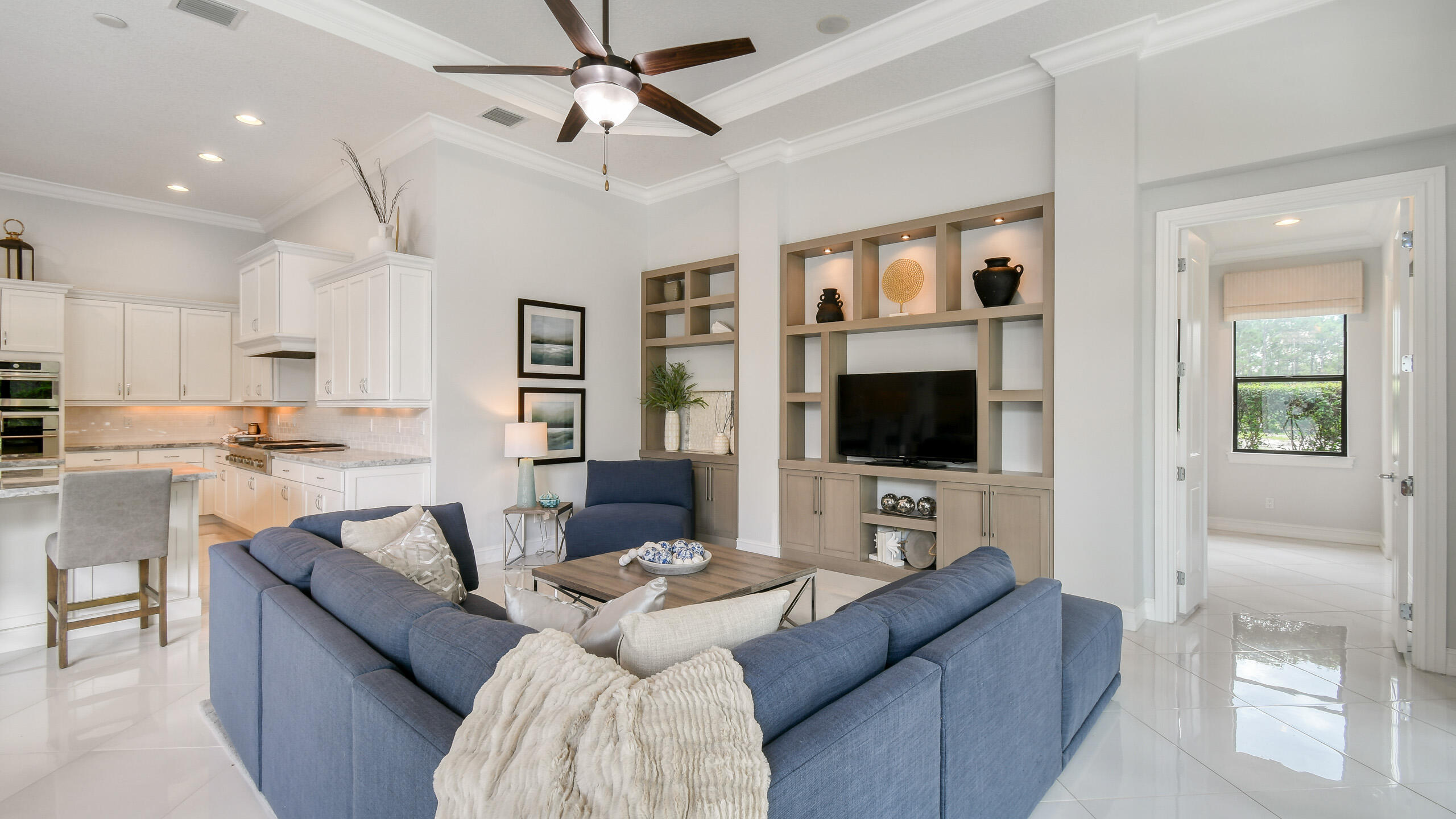 Open-plan living room with blue sectional, built-in media shelves, and adjoining white kitchen.