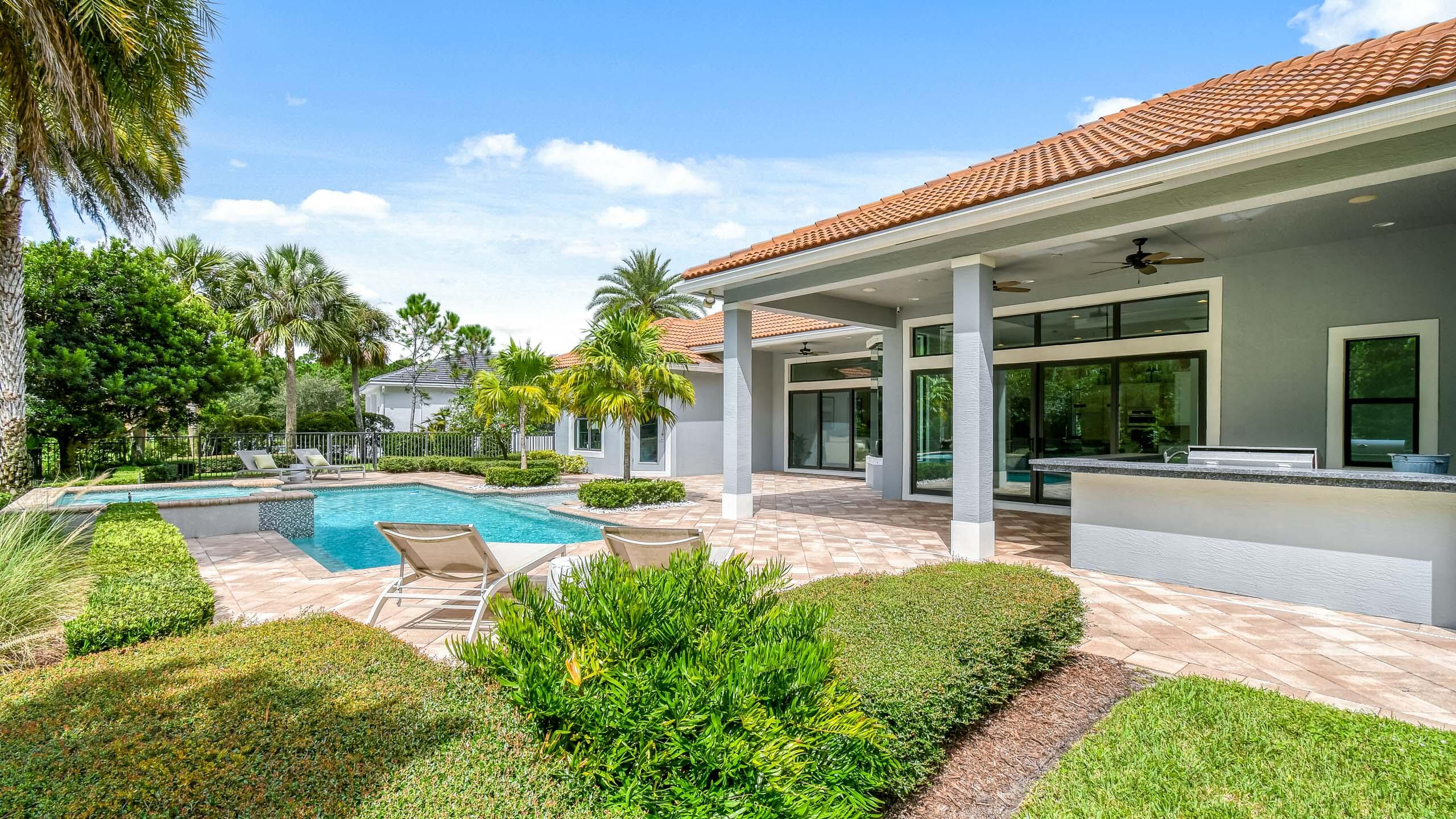 Modern home’s covered patio and outdoor kitchen beside a curved pool and landscaped yard.
