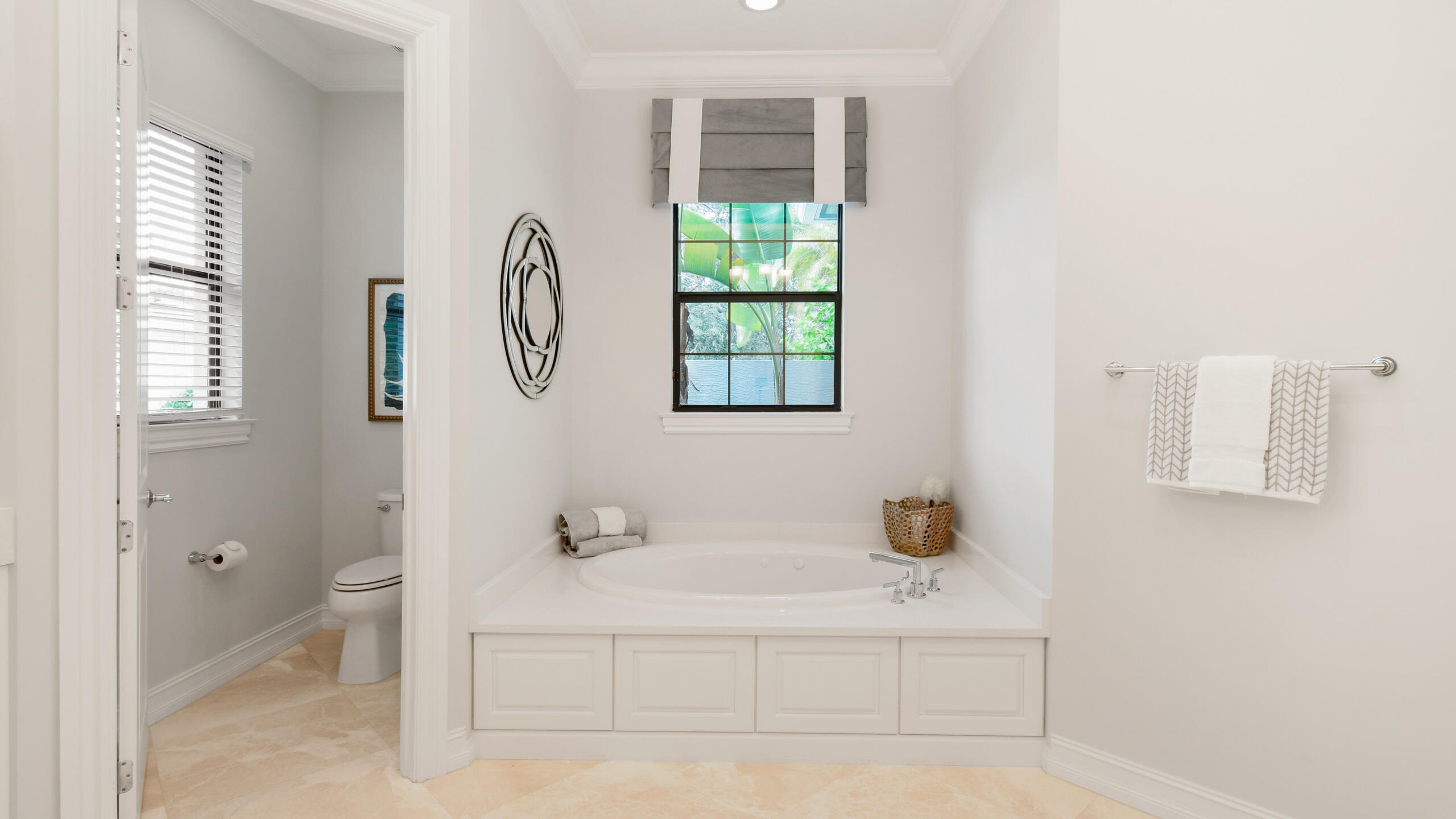 Bathroom with a built-in soaking tub beneath a window overlooking greenery and an adjoining toilet alcove.