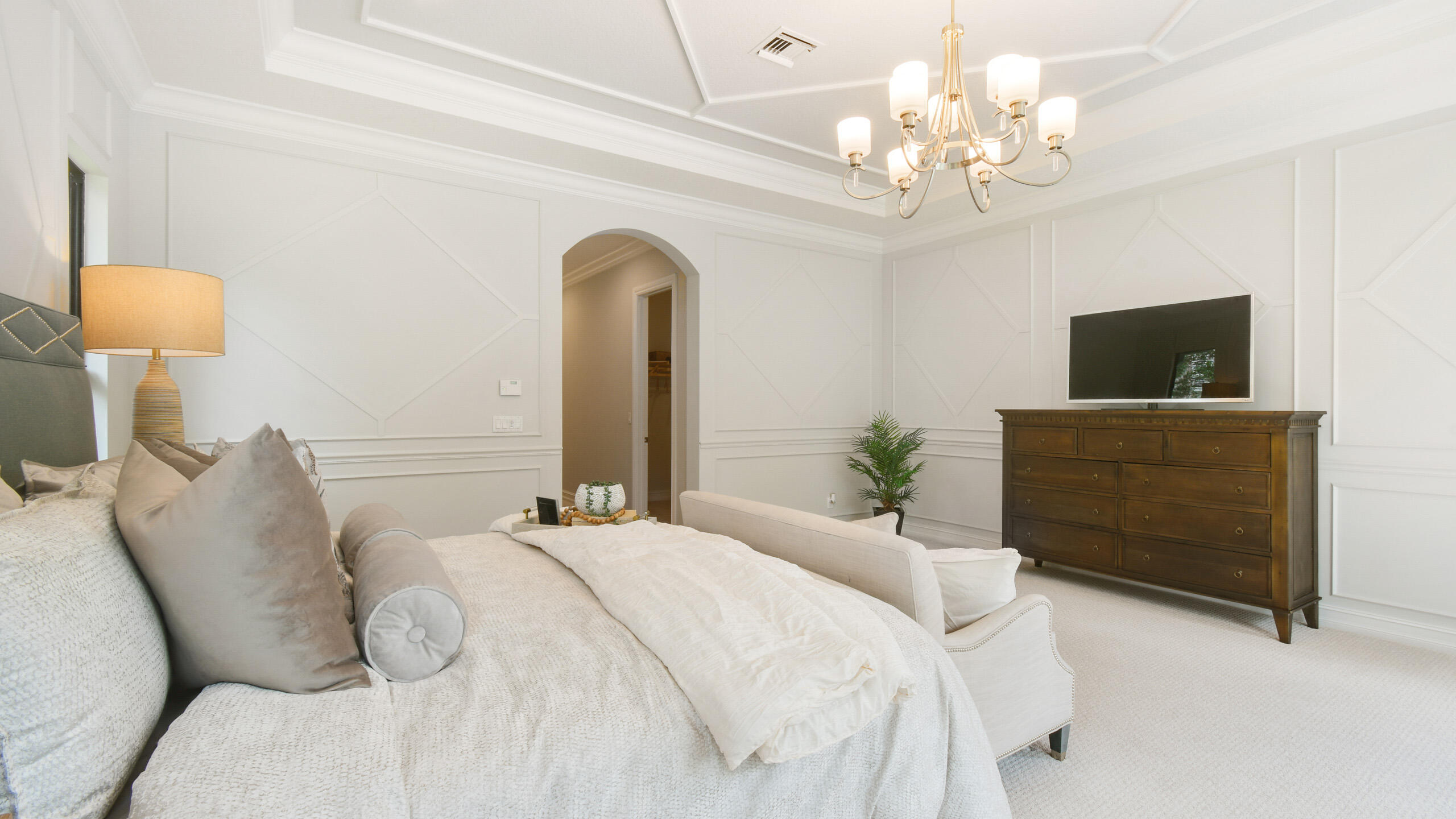 Bright bedroom with a large upholstered bed, geometric wall paneling, and a TV on a dark wood dresser.