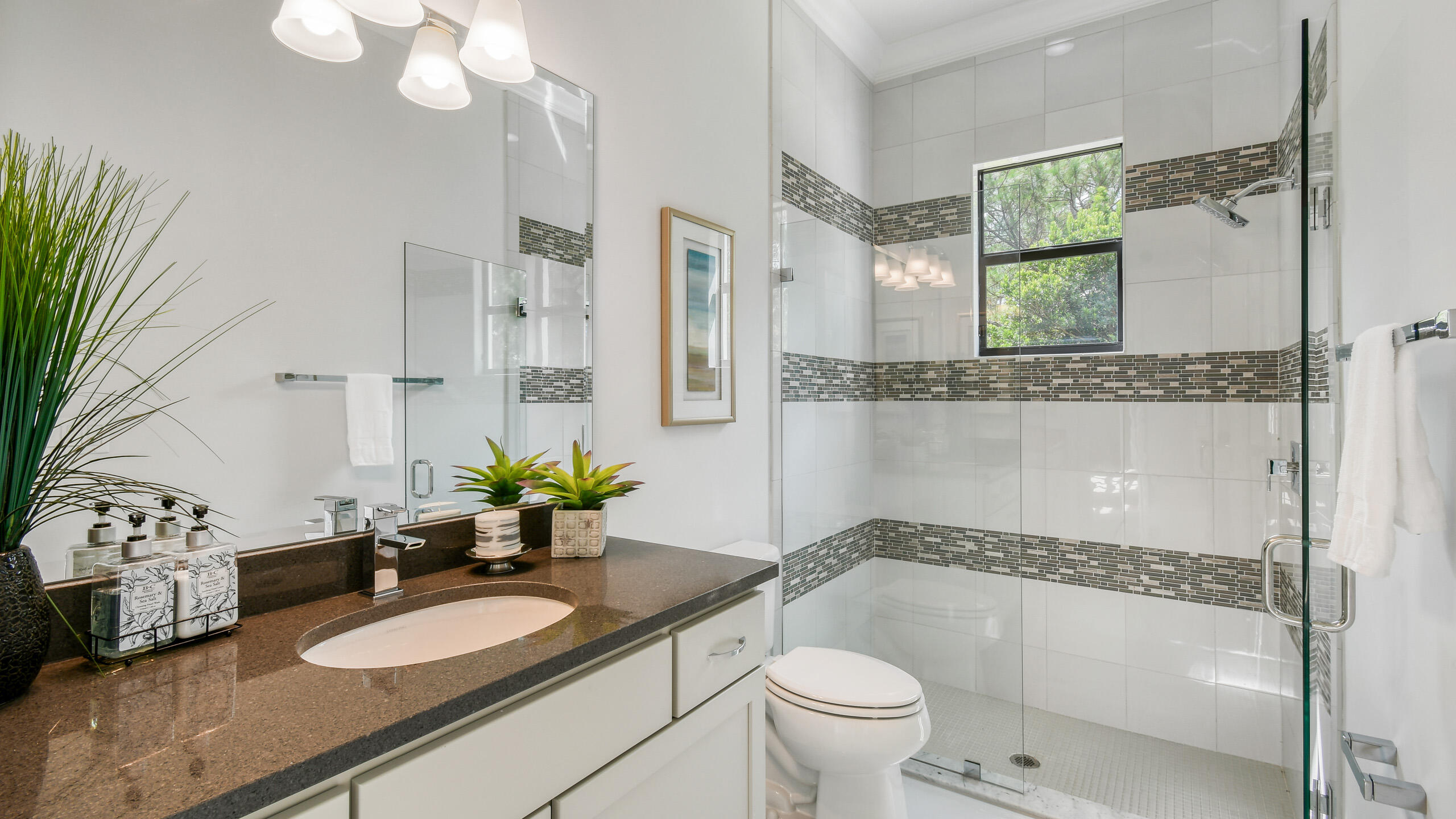 Bathroom with a dark stone vanity and a glass shower accented with horizontal mosaic tile bands.
