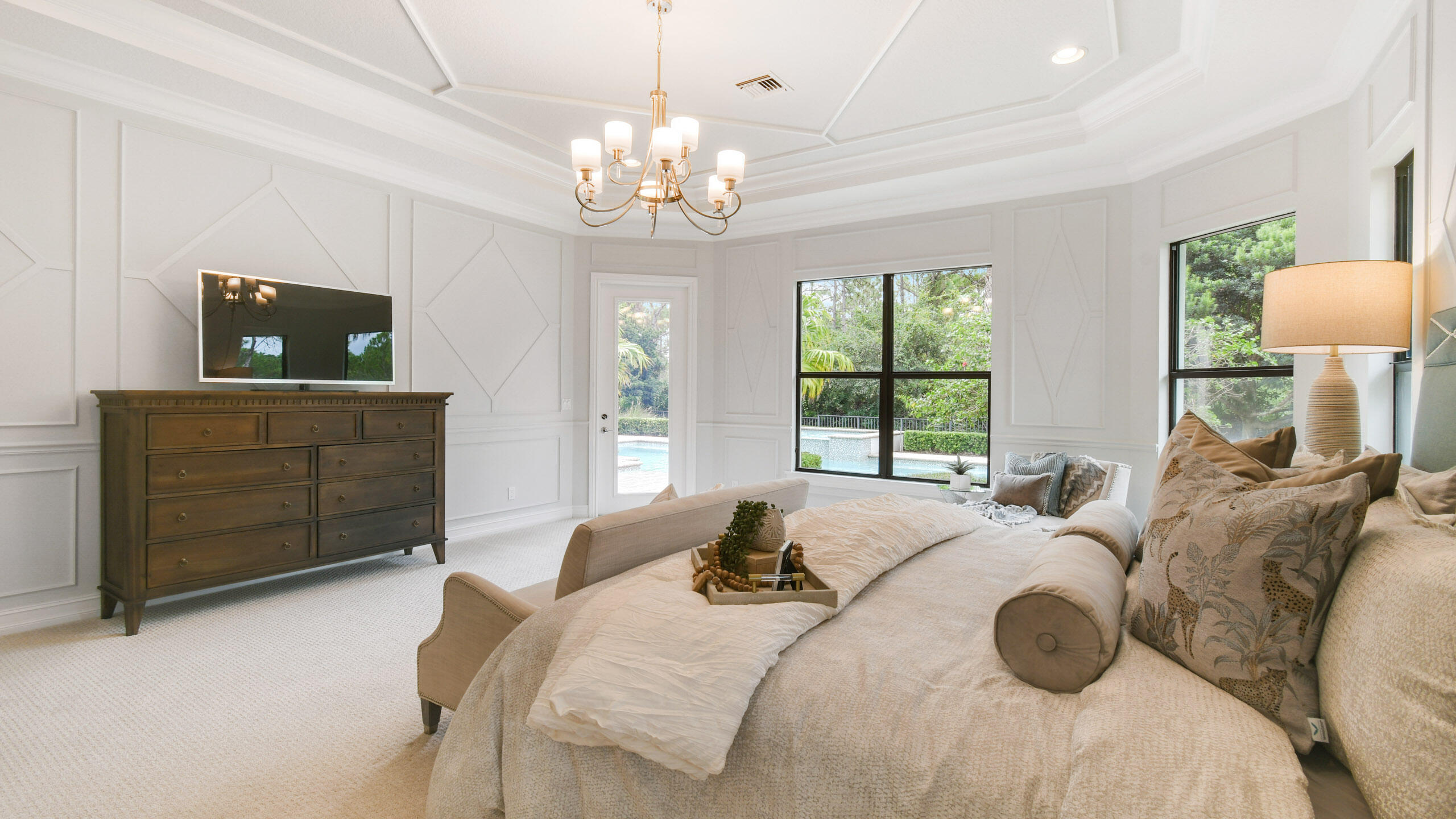 Bedroom with a large upholstered bed, paneled walls, and windows overlooking a pool.