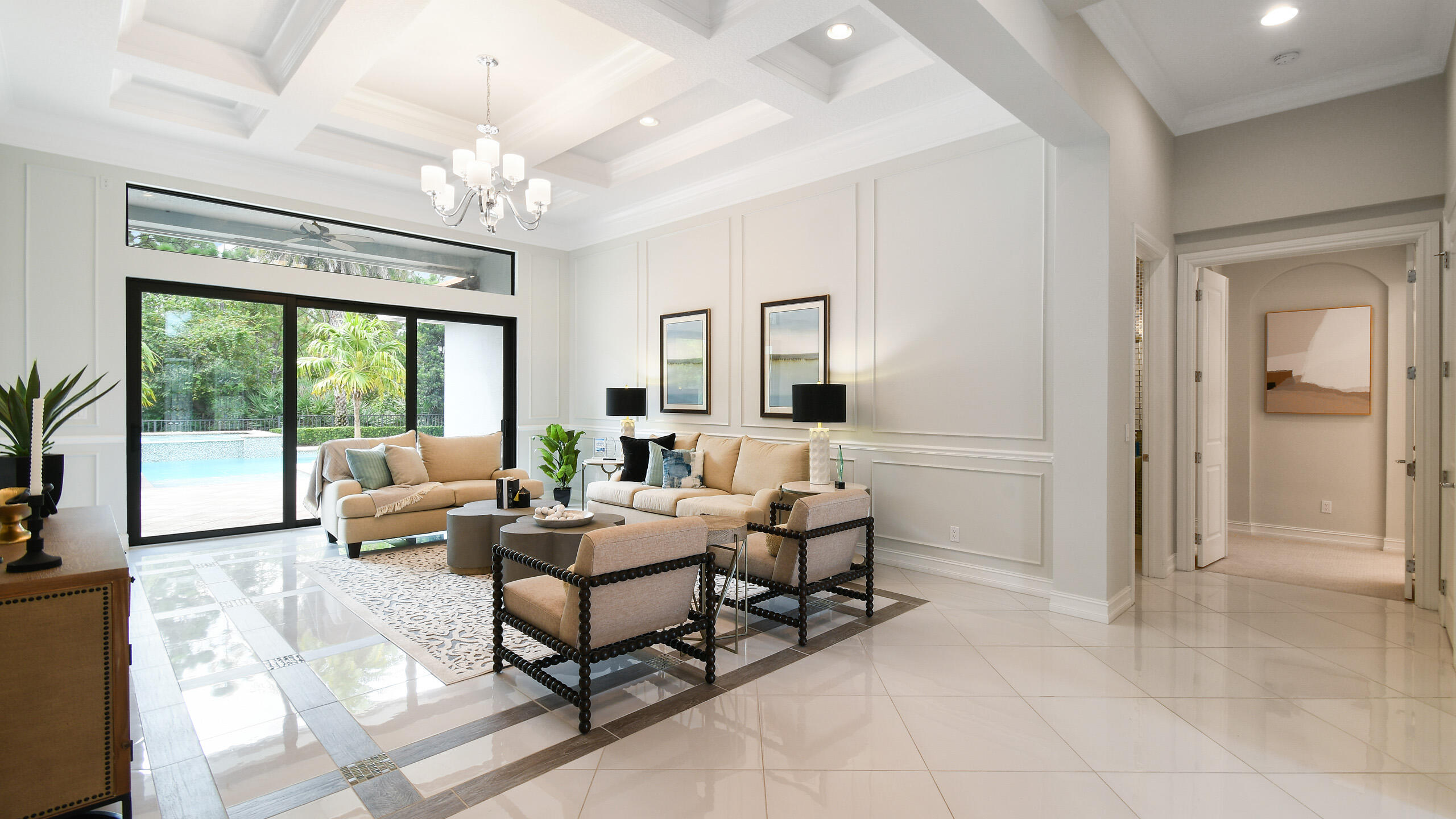 Furnished living room with a coffered ceiling and sliding doors overlooking a pool.