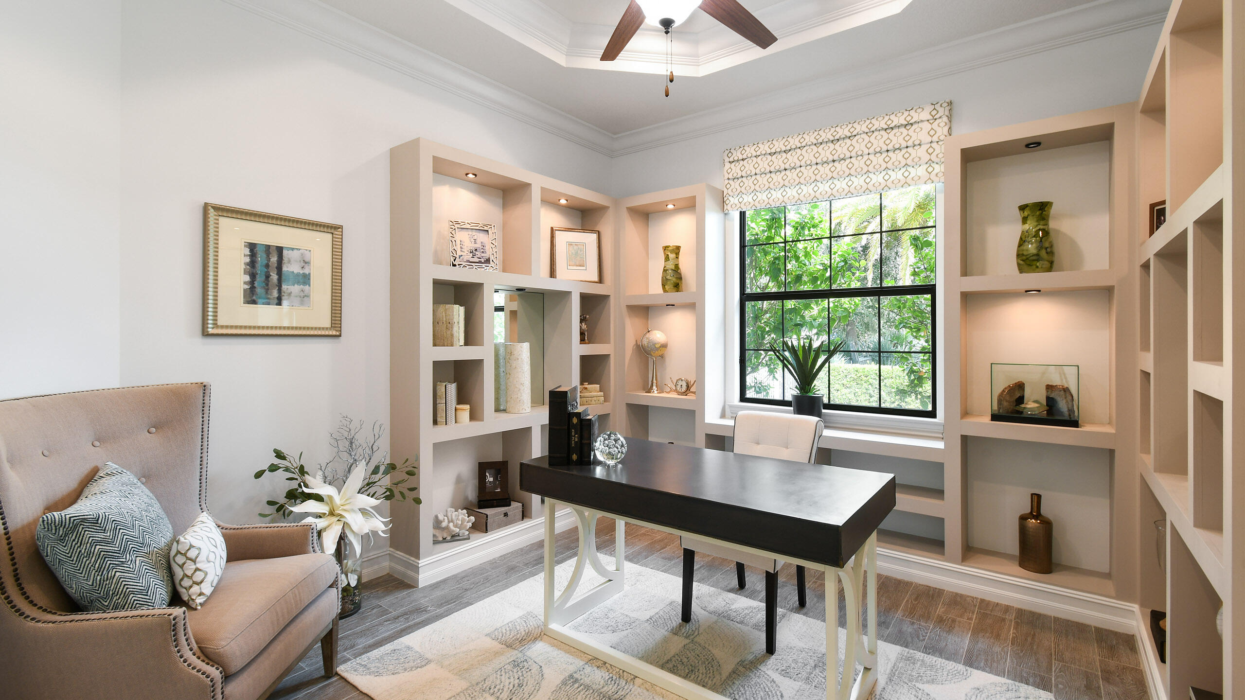 Home office with built-in shelves, a dark desk, and a large window overlooking greenery.