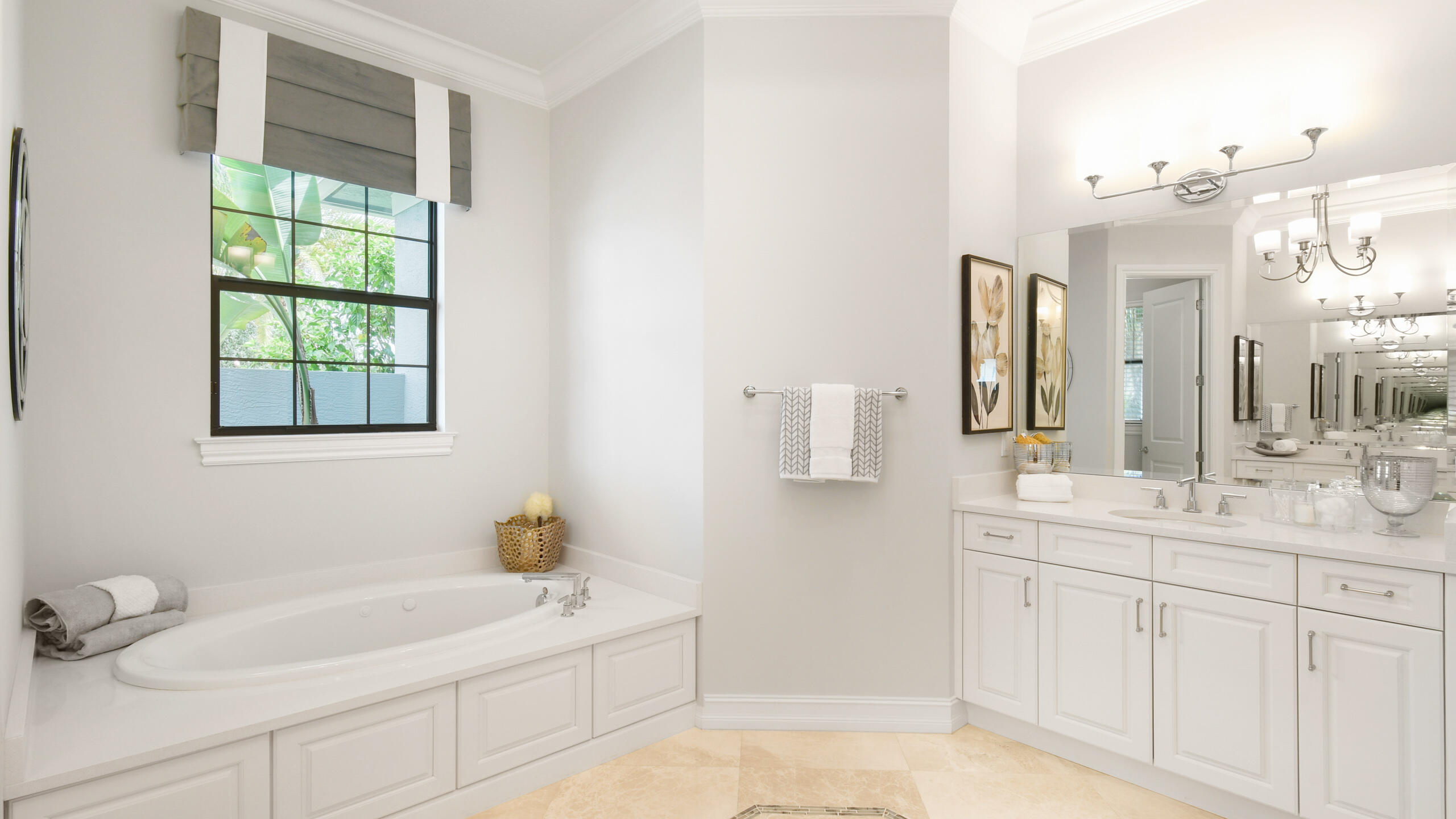 Bright bathroom with a built-in soaking tub beneath a window and a white vanity with a large mirror.