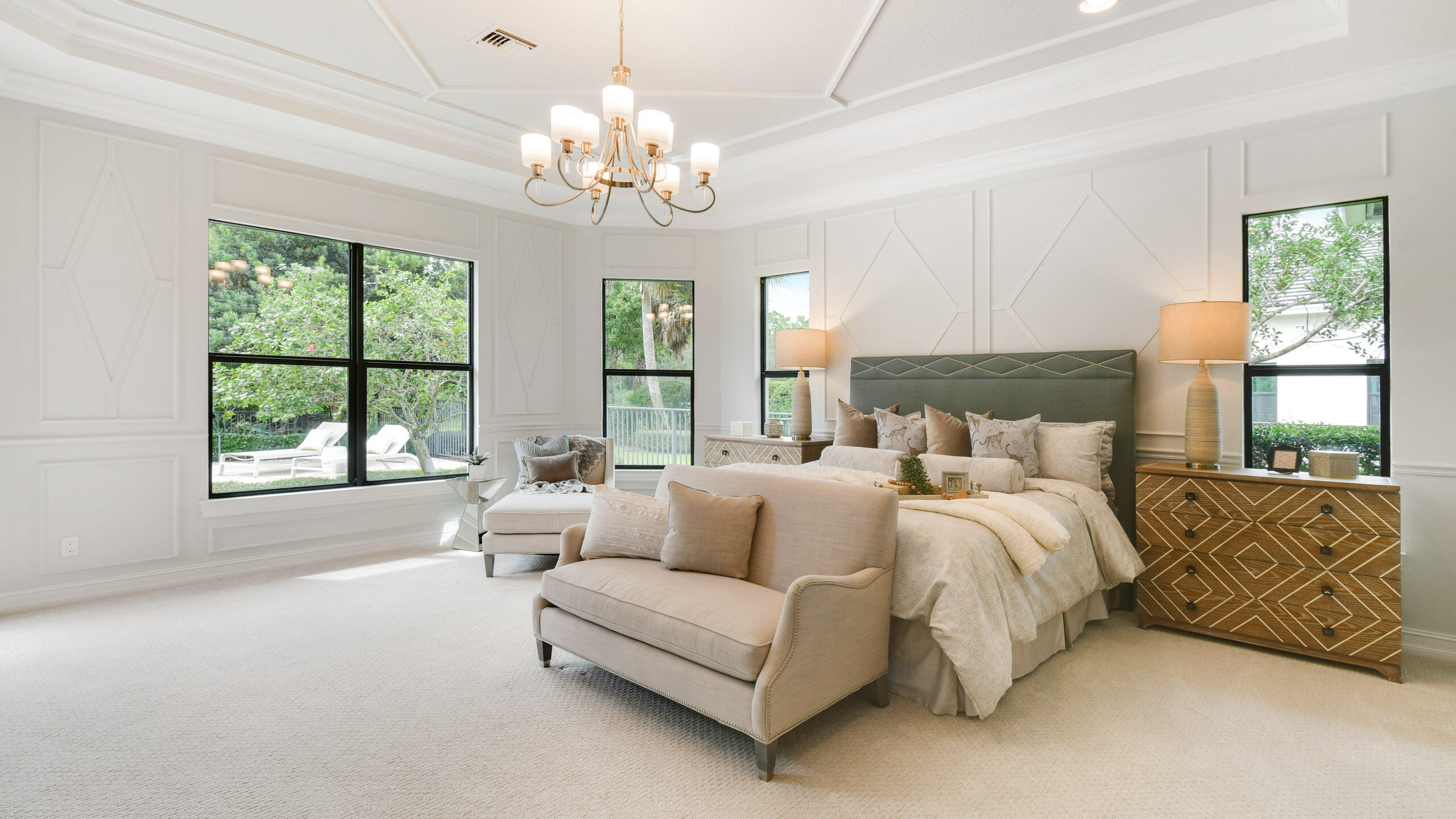 Bright bedroom with a king-size bed, upholstered bench, and large windows overlooking greenery.
