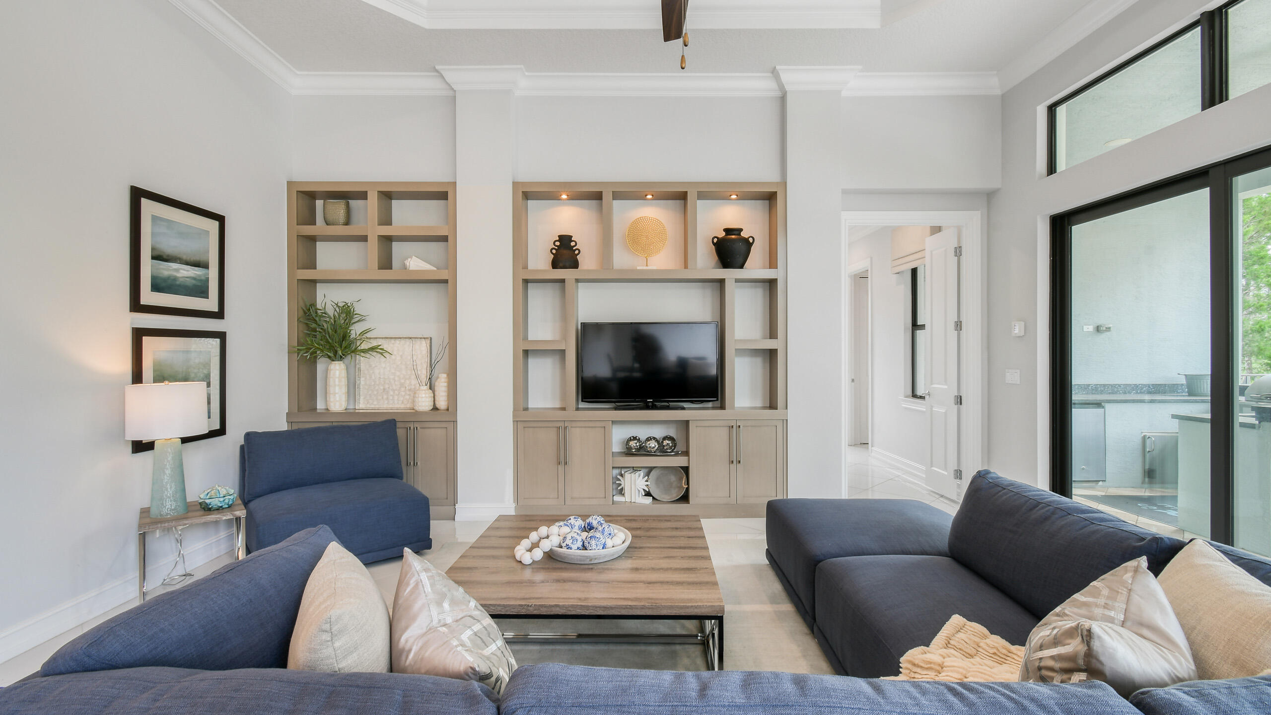 Living room with blue seating, built-in TV shelving, and tall windows opening to a patio.