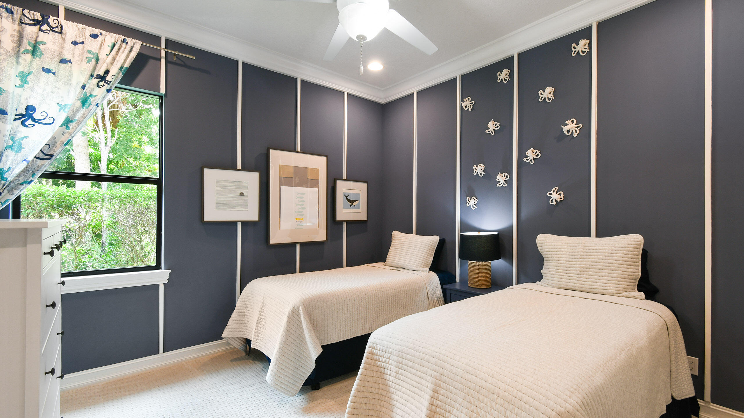 Twin-bed bedroom with navy paneled walls, shell decorations, and a bright garden-facing window.
