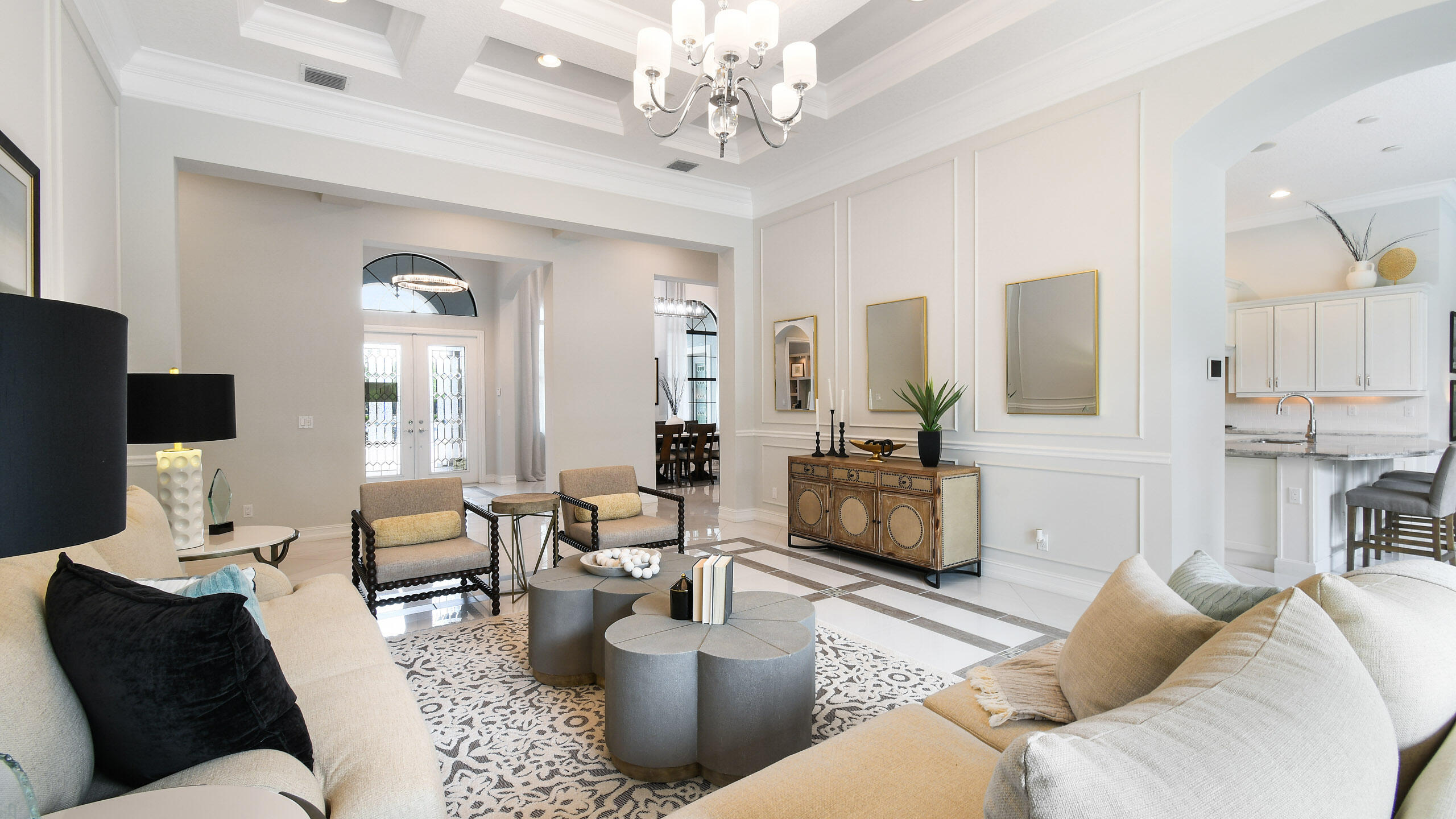 Living room with cream sofas, sculptural coffee tables, a patterned rug, and the dining area and kitchen beyond.