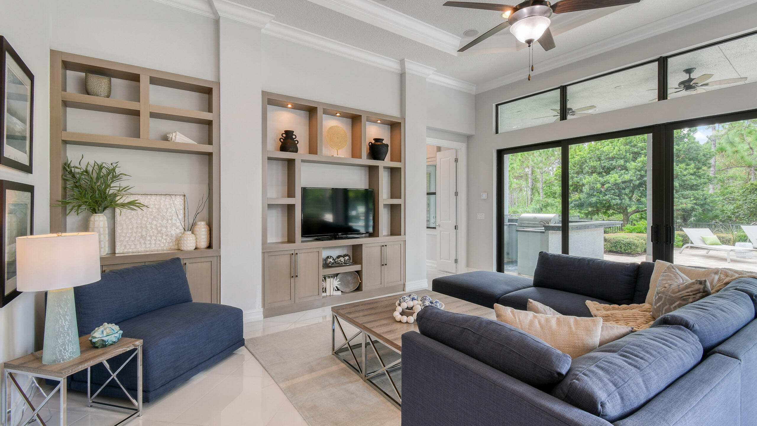 Living room with built-in shelving, navy sofas, and glass doors opening to a leafy patio.