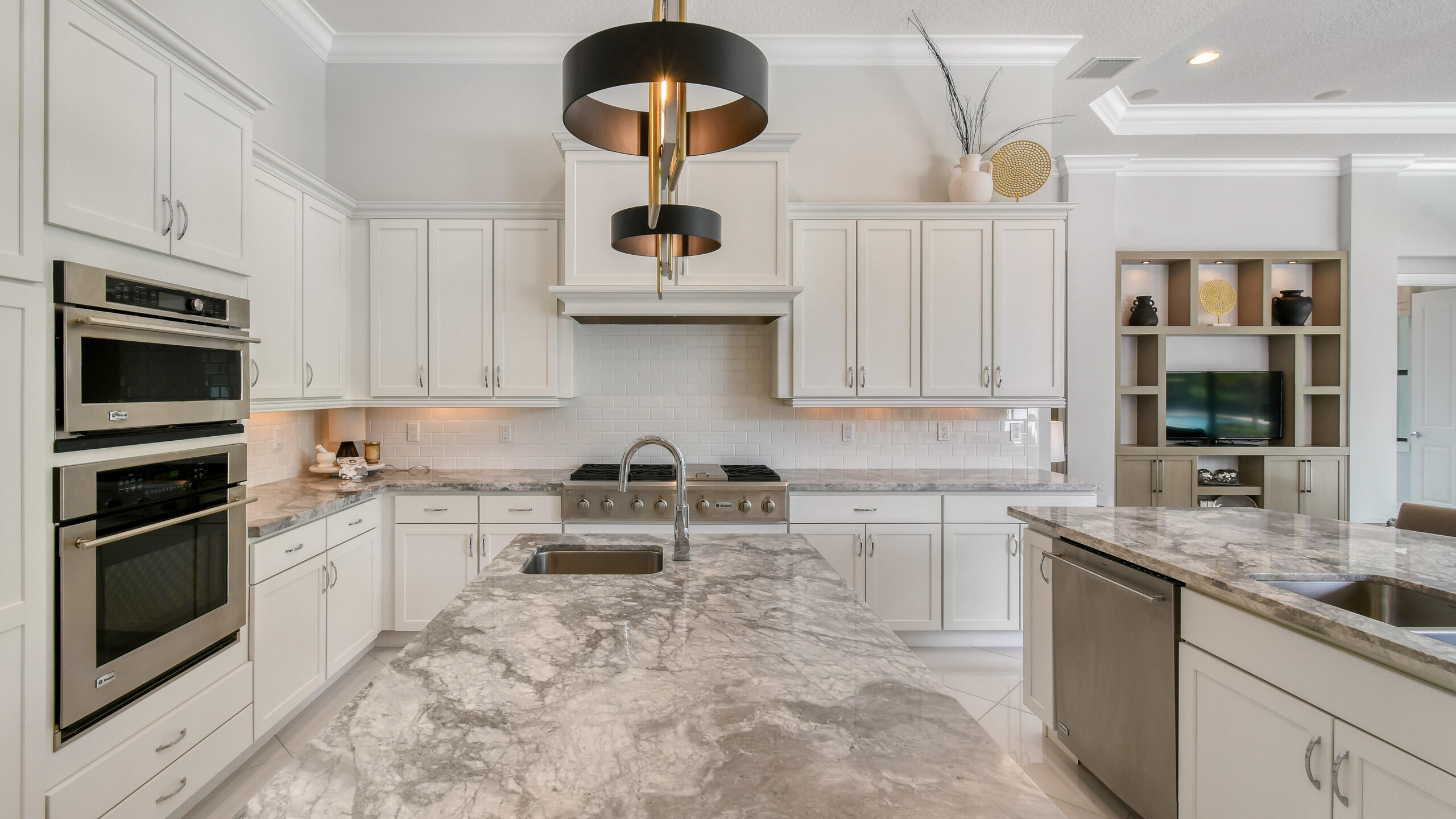 Kitchen with a large marble island, white cabinetry, stainless steel double ovens, and a built-in cooktop.