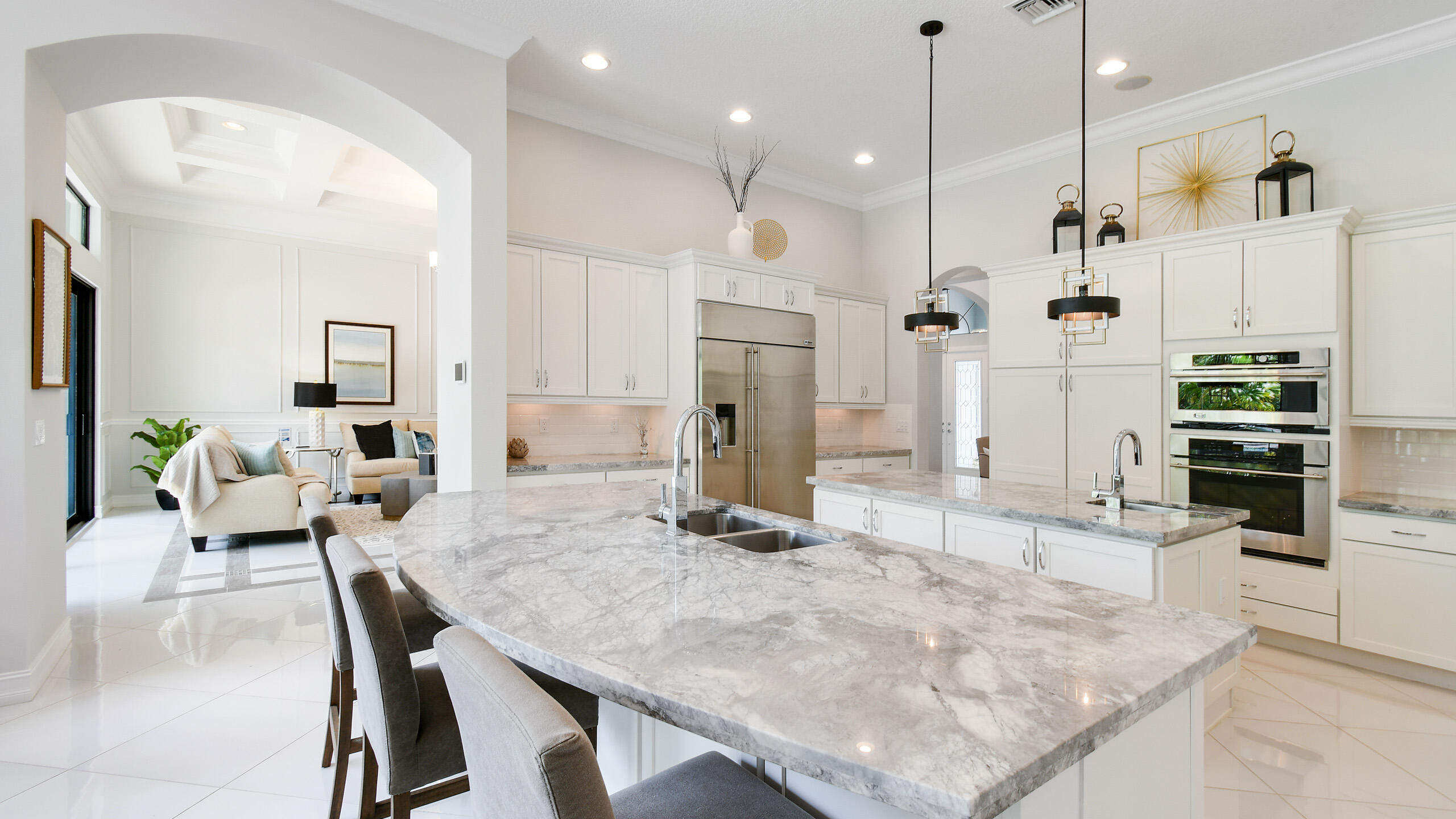 Bright kitchen with a large veined marble island, white cabinetry, and stainless steel appliances.