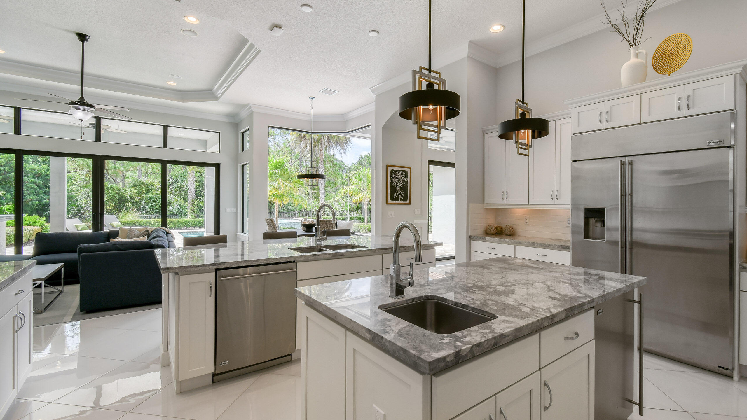 Open-plan kitchen with a large stone island, stainless steel appliances, and windows overlooking tropical greenery.