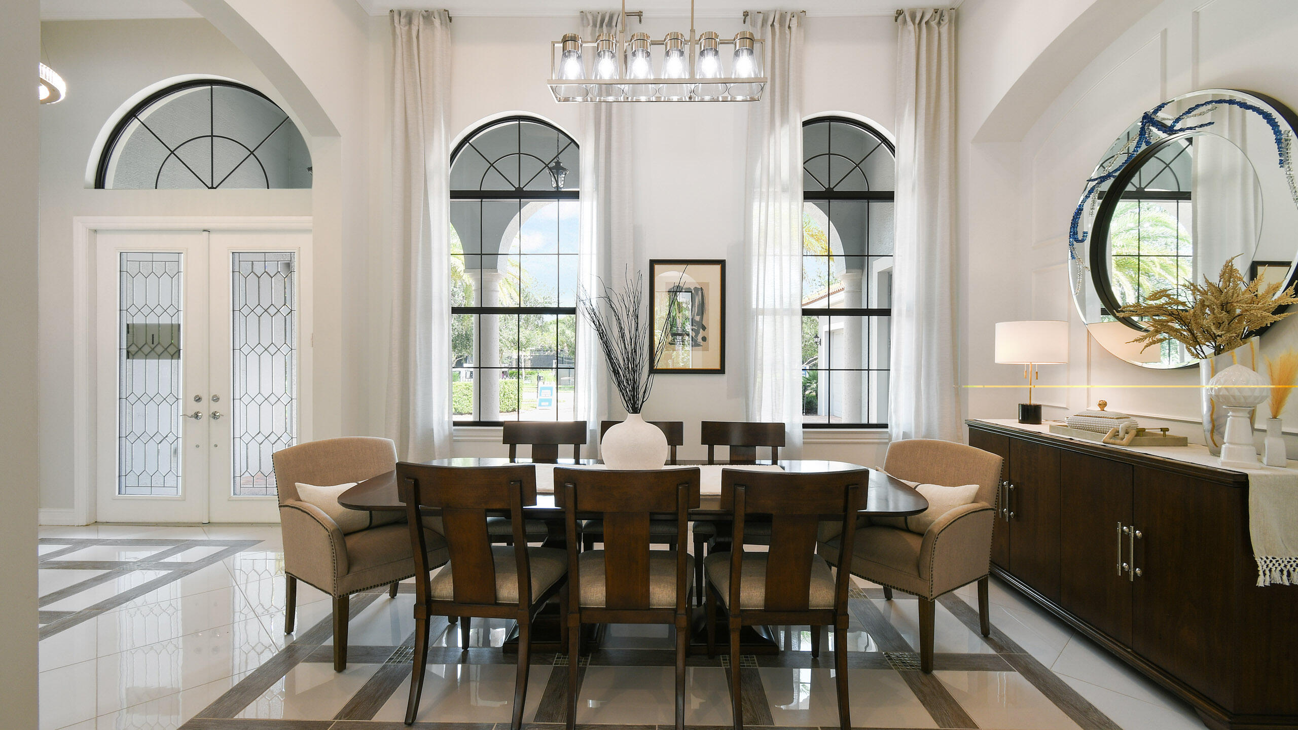 Dining room with a dark wood table beneath tall arched windows and a glass-paneled entry door.