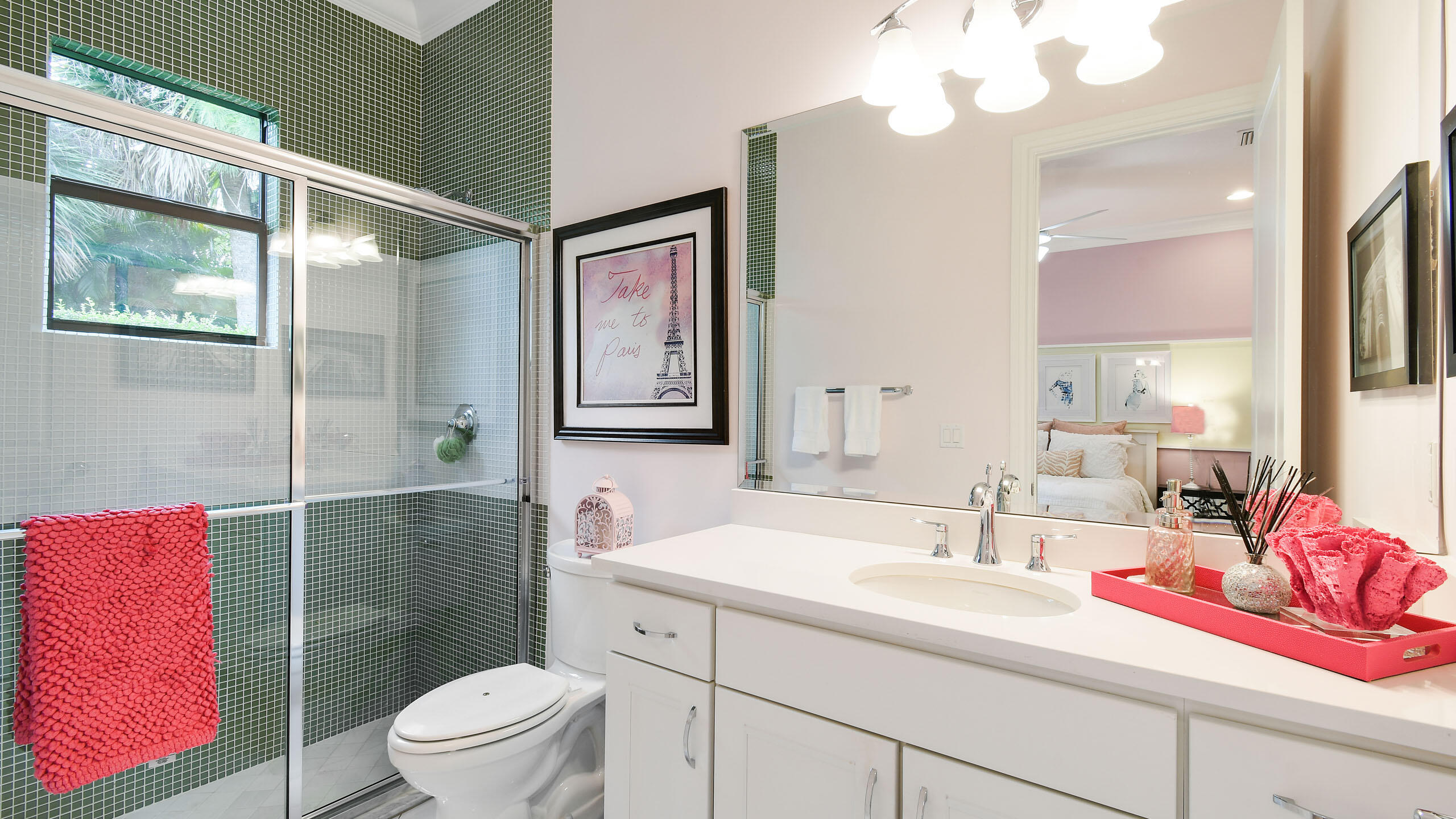 Bathroom with a green mosaic-tile shower, white vanity, and window overlooking greenery.