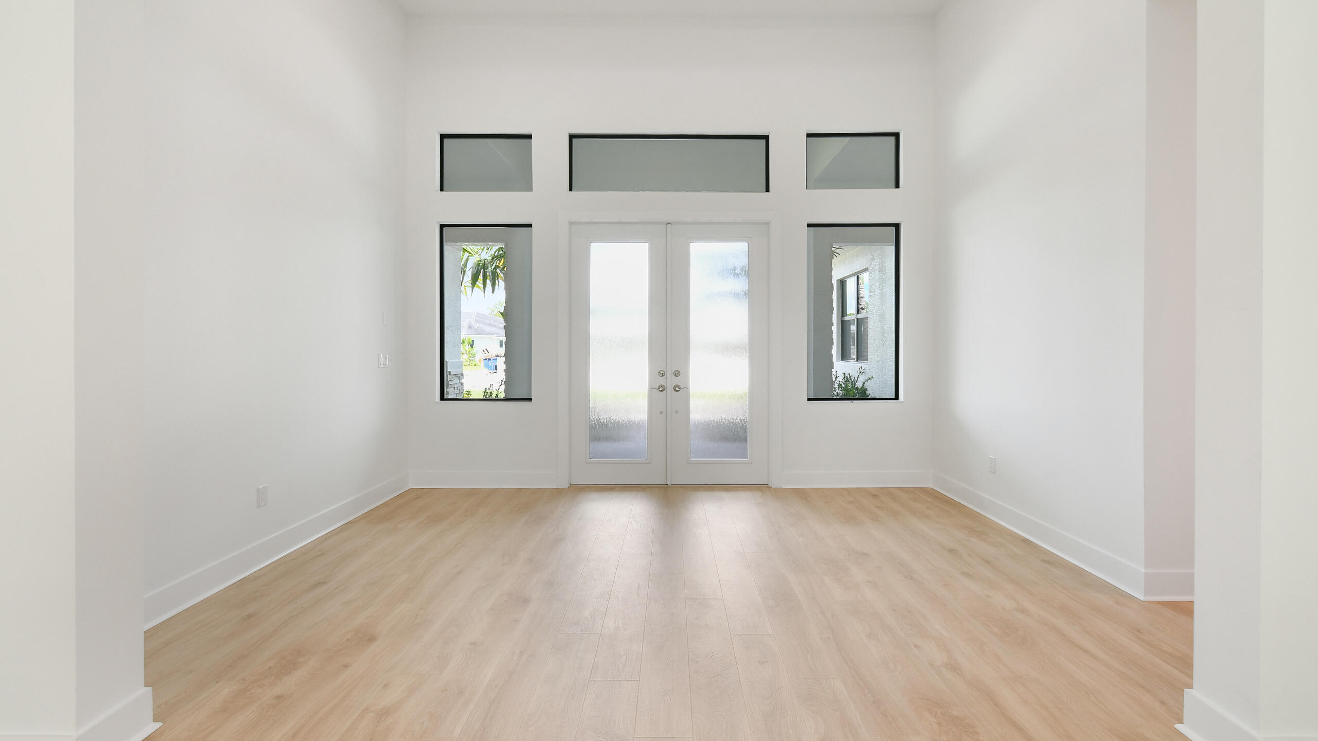 Empty entry foyer with light wood floors and double glass front doors.