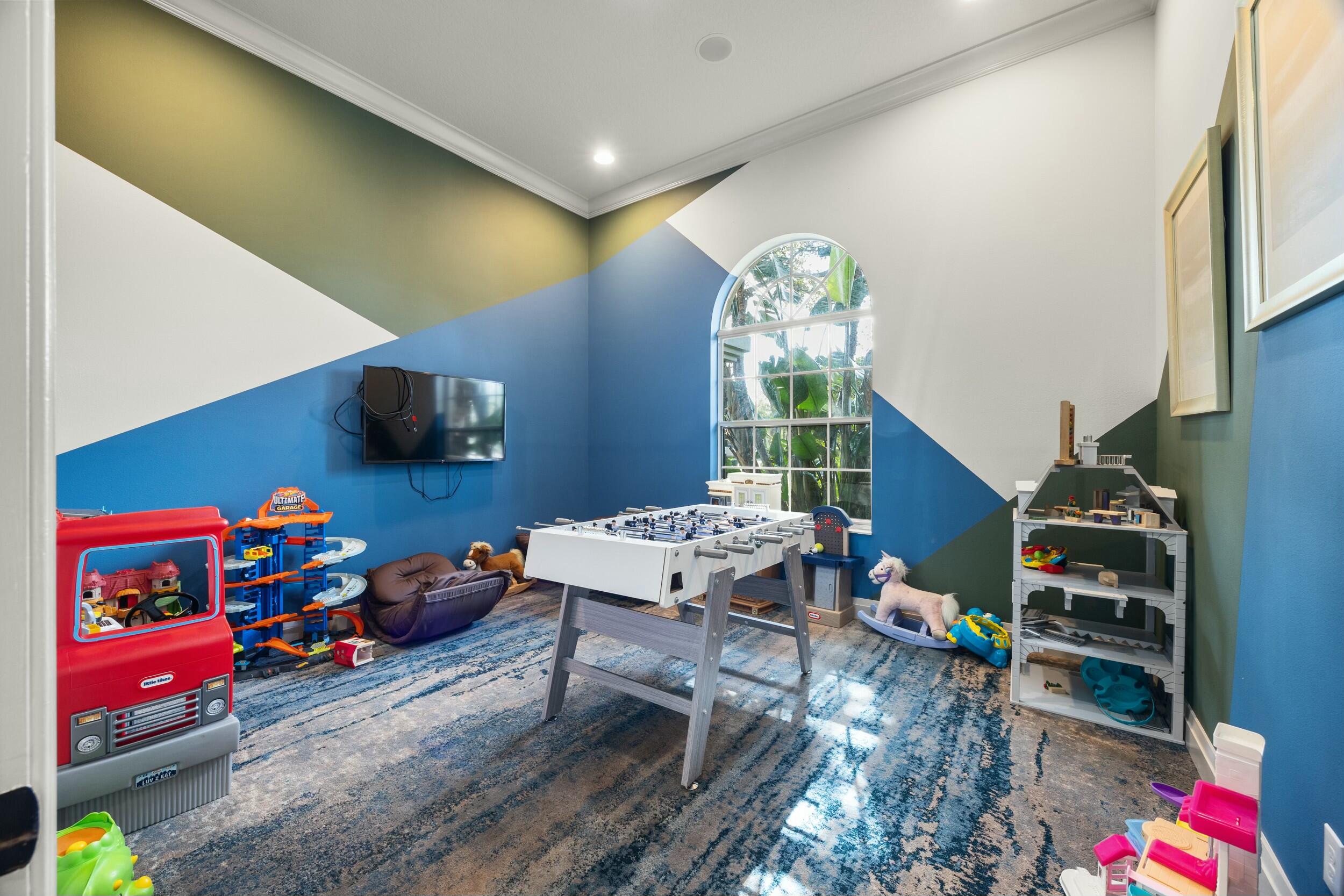 Playroom with a foosball table, colorful toys, geometric walls, and a tall arched window.