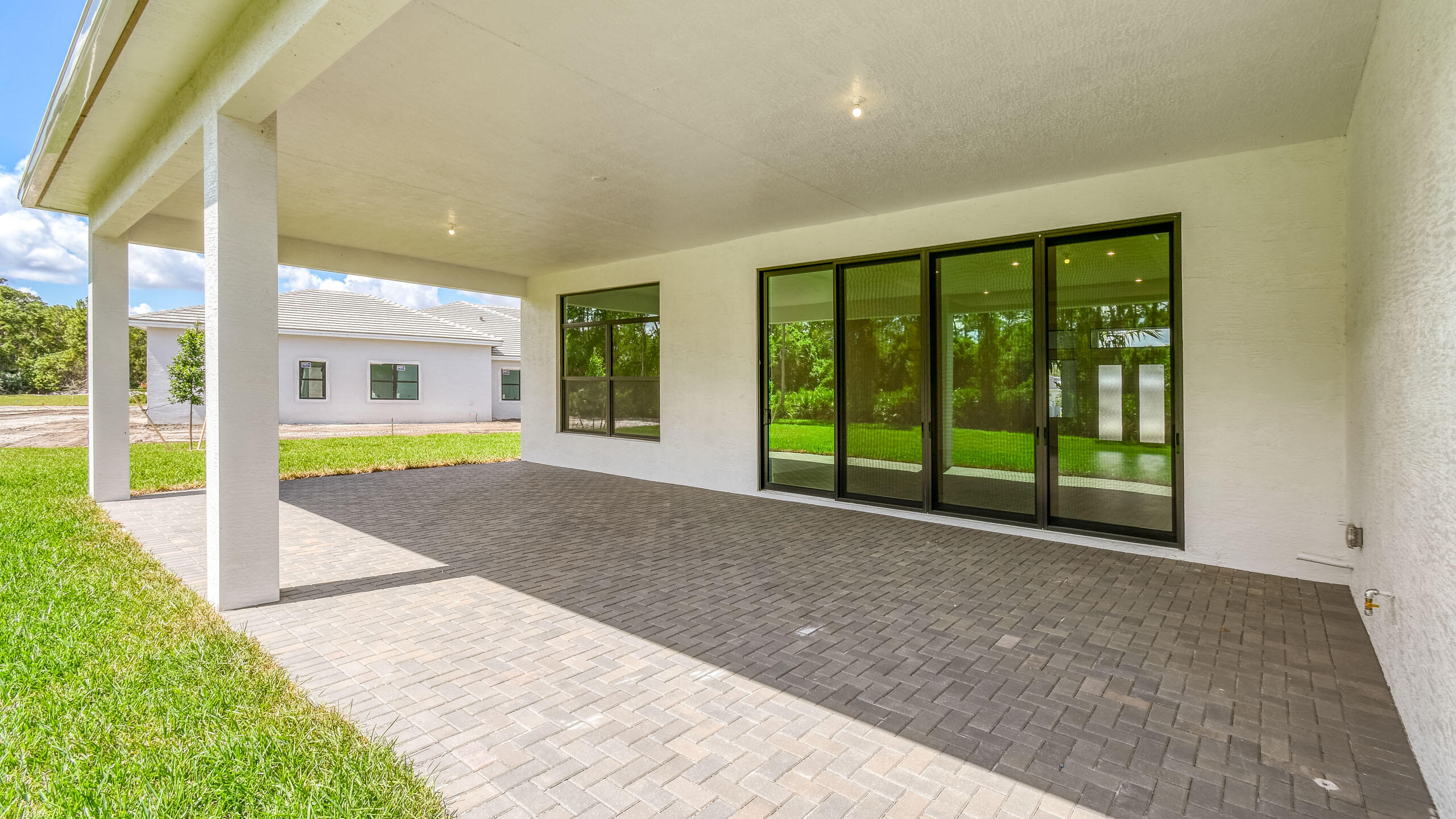 Covered rear patio with gray pavers, white columns, and large sliding glass doors facing a green lawn.