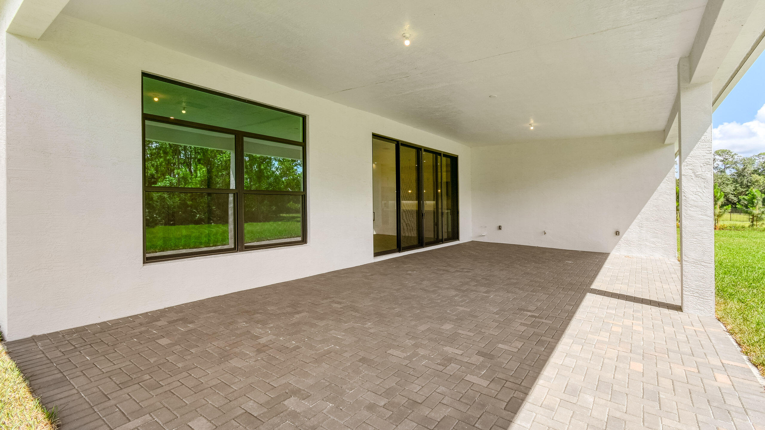 Covered rear patio with brown pavers, large windows, sliding glass doors, and a view of the lawn.