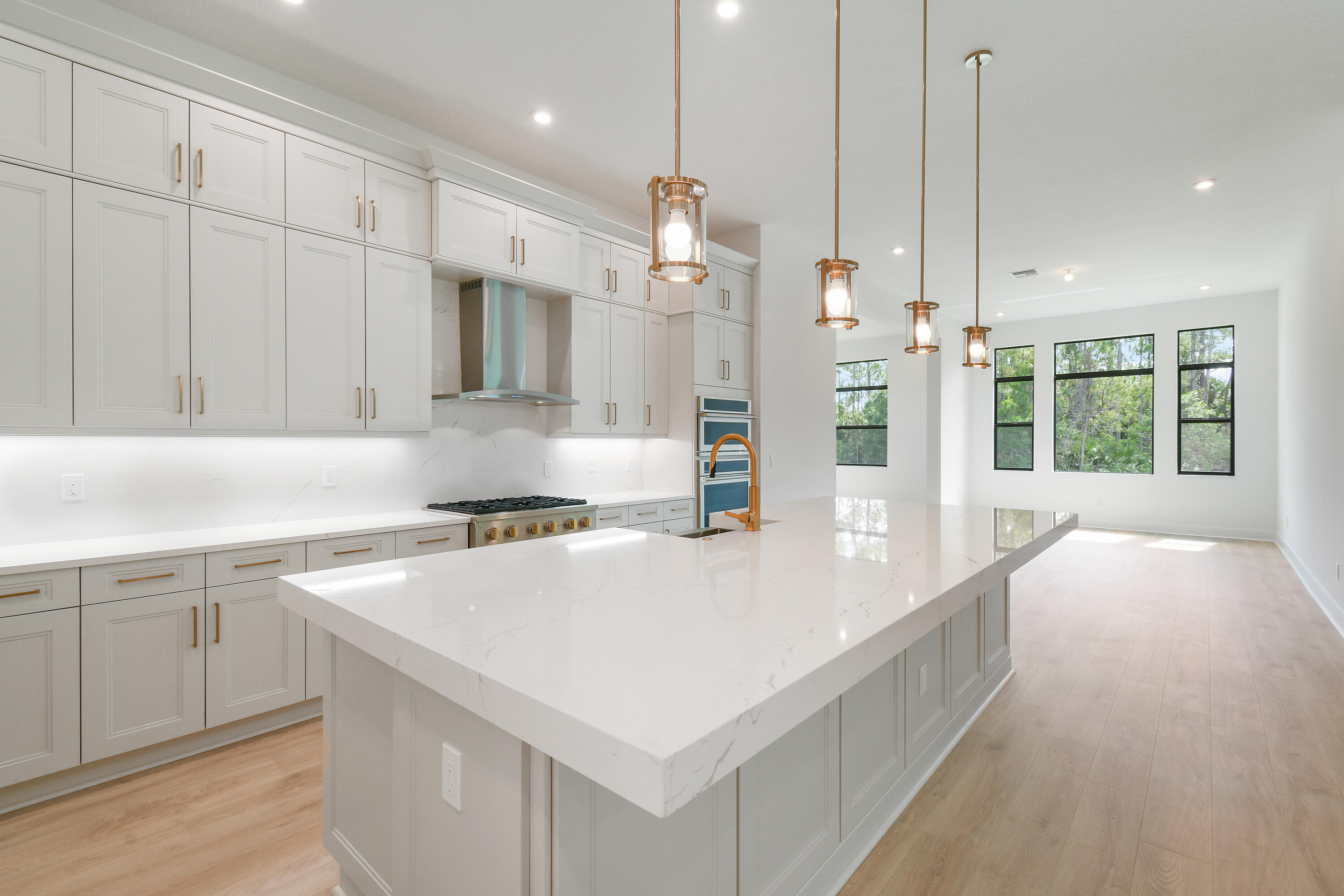 Modern kitchen with a large veined stone island, white cabinetry, brass fixtures, and tall windows.