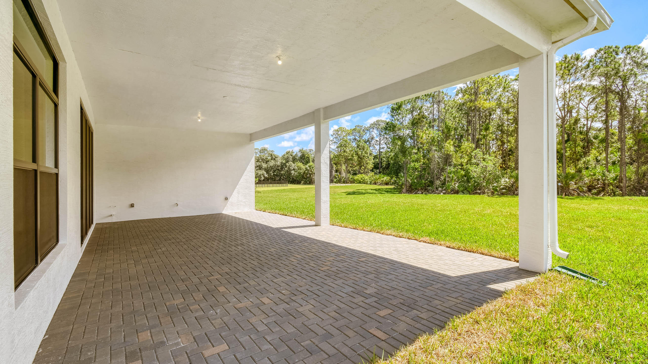 Covered paver patio opening onto a green lawn and wooded backyard.