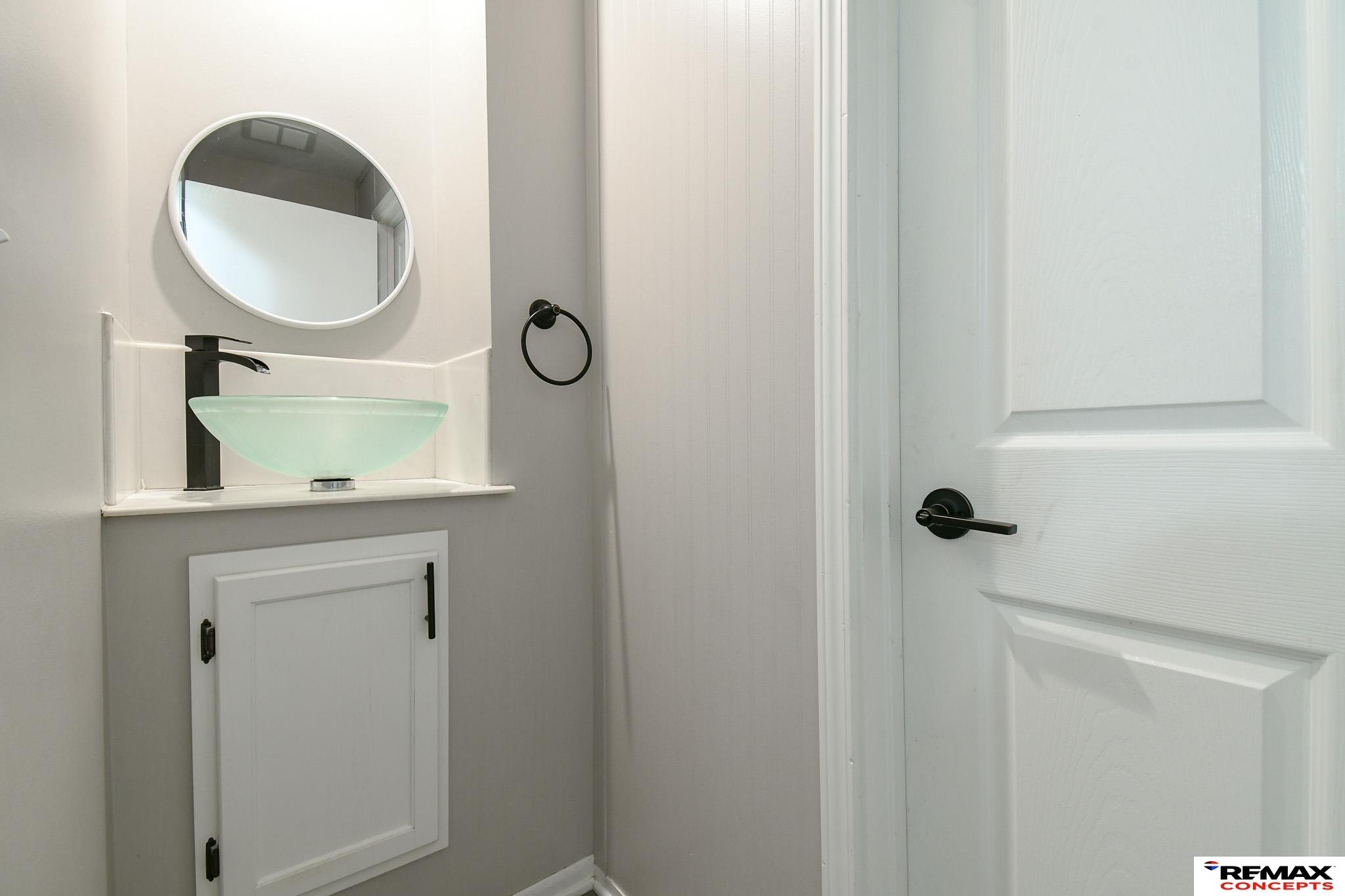 Bathroom vanity with a pale green vessel sink, black faucet, and round mirror.