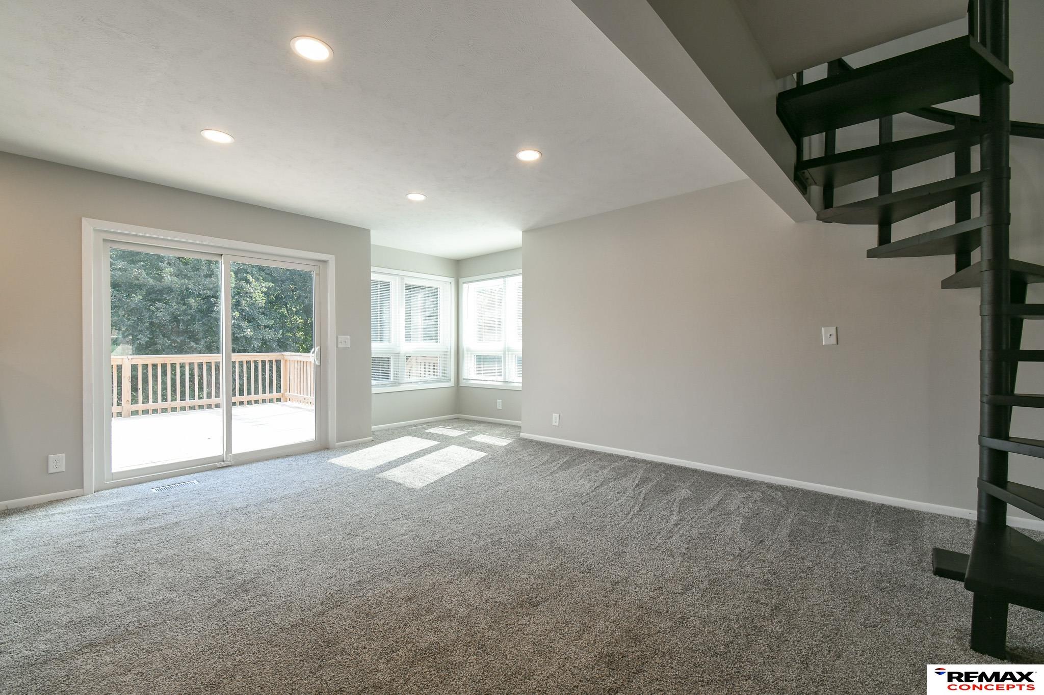 Vacant living room with gray carpet, a black spiral staircase, and sliding glass doors to a deck.
