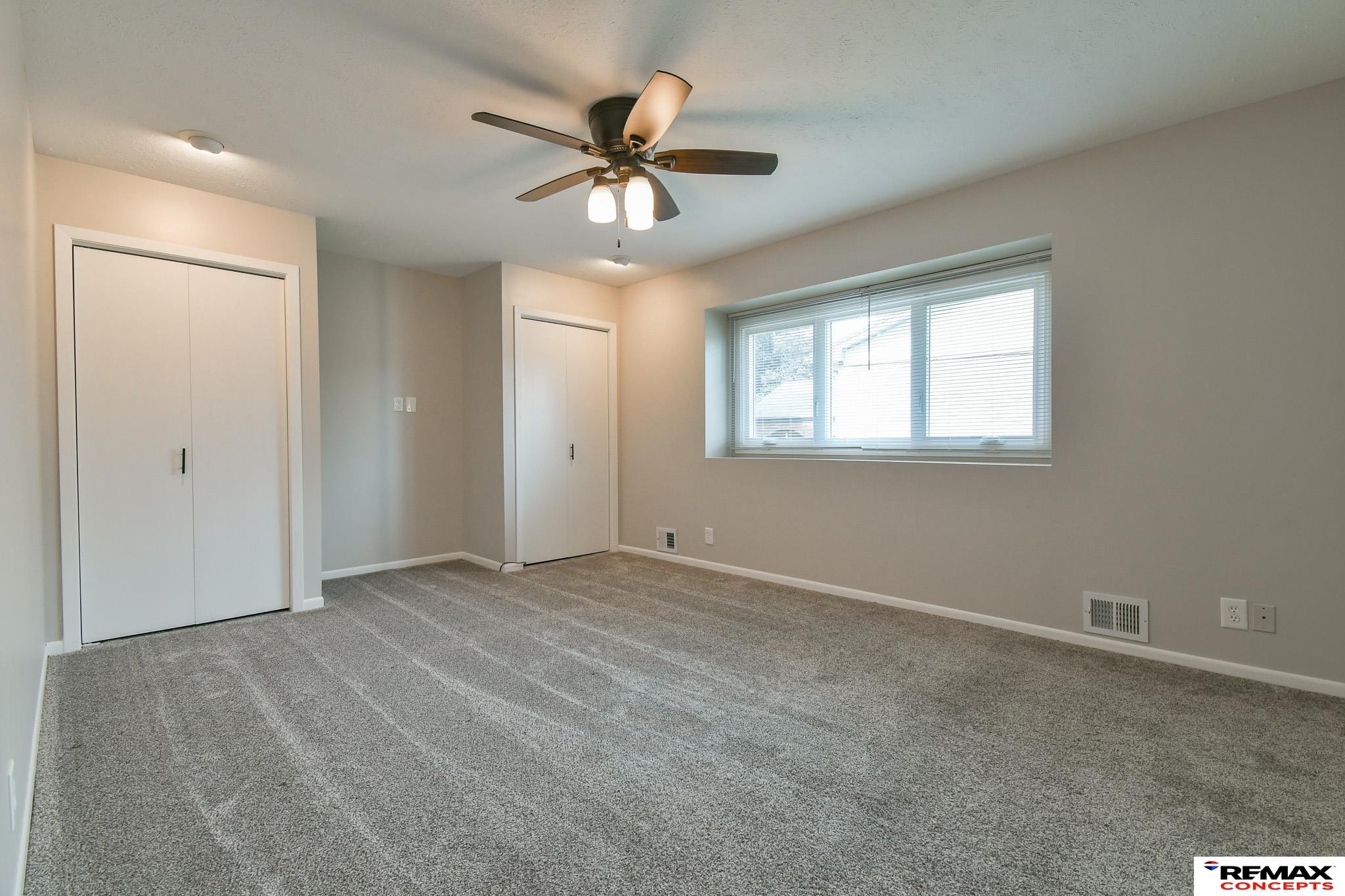 Empty carpeted bedroom with a closet, window, and ceiling fan.